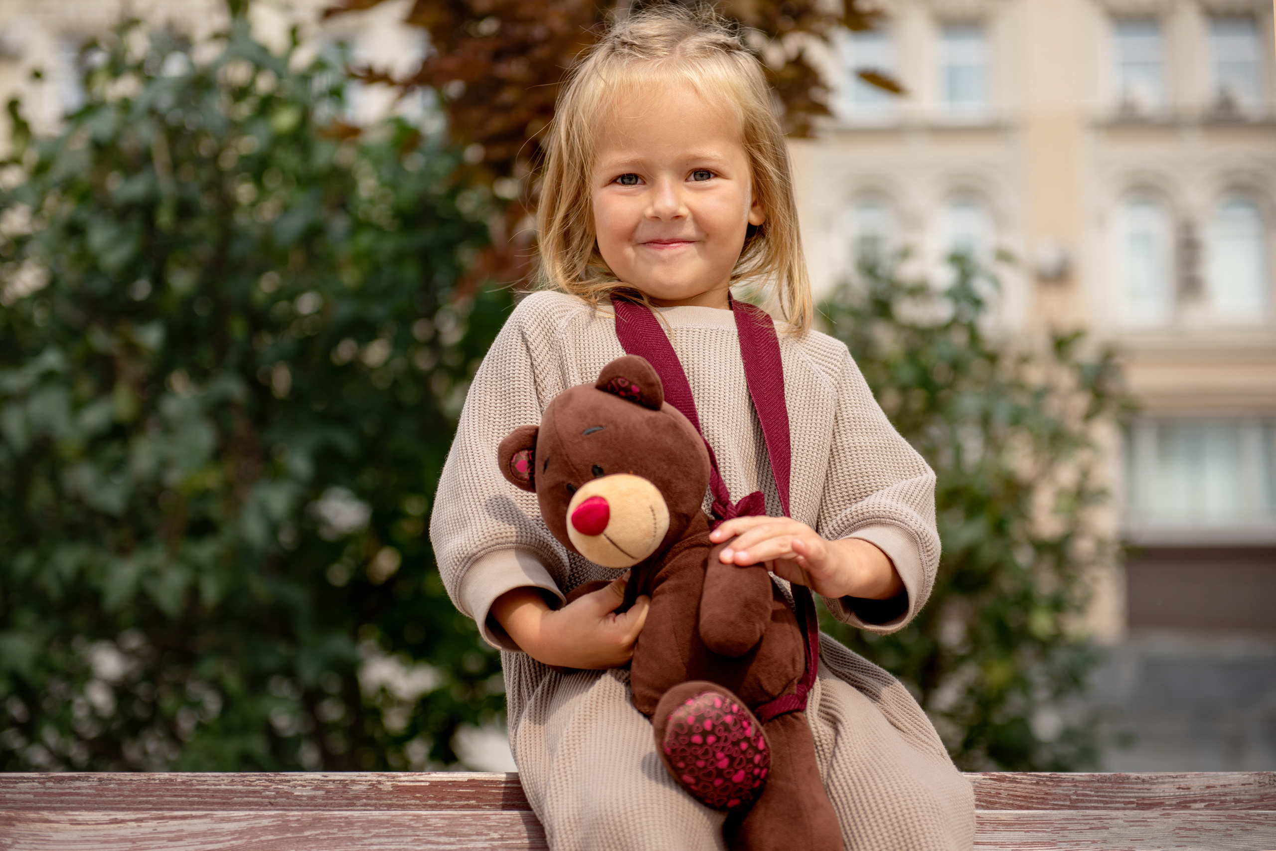 Девочка с любимой игрушкой мишкой сидит на скамейке