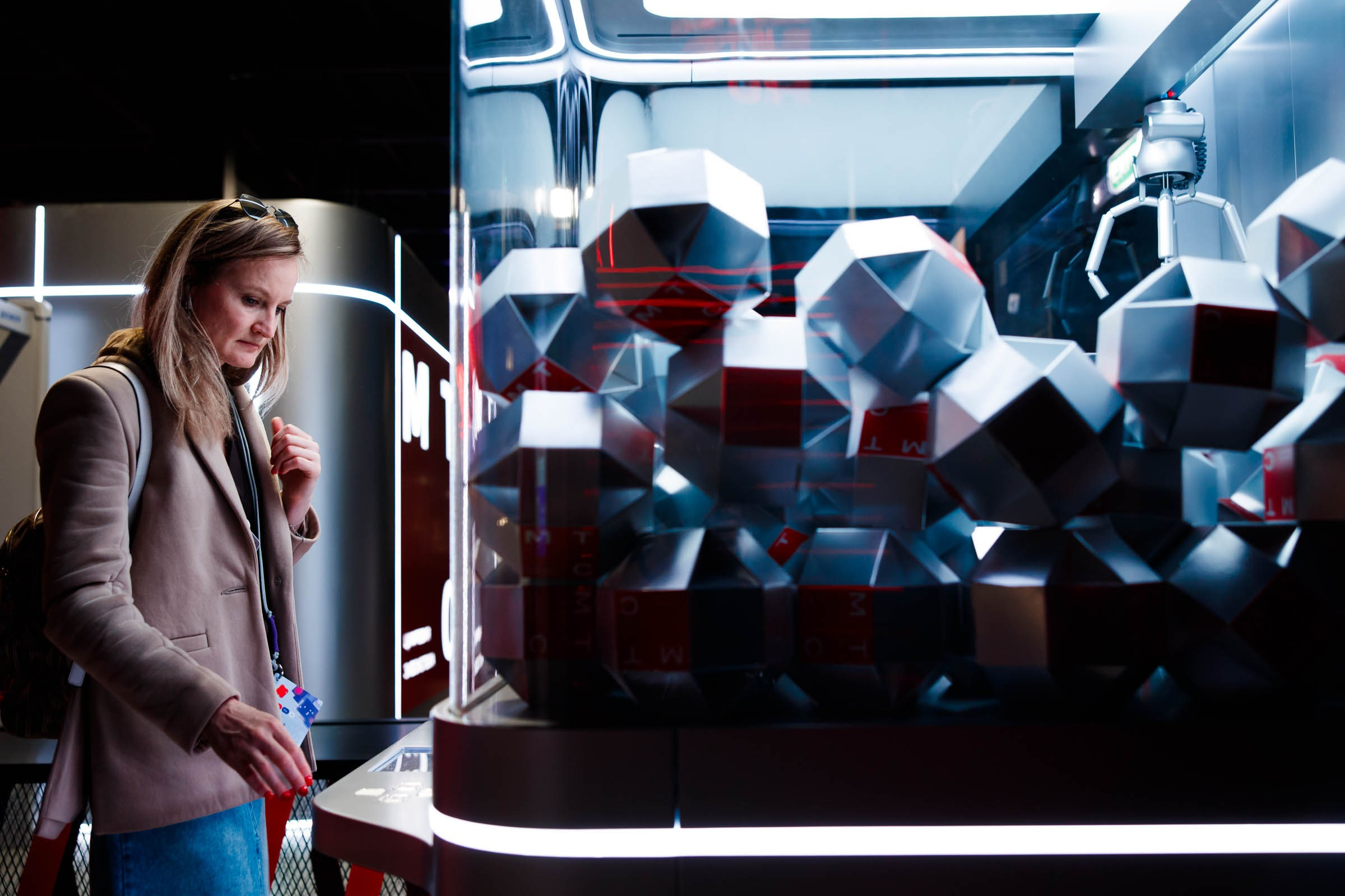 Посетительница форума рассматривает футуристическую инсталляцию из многогранников, интерьерная съемка площадки.