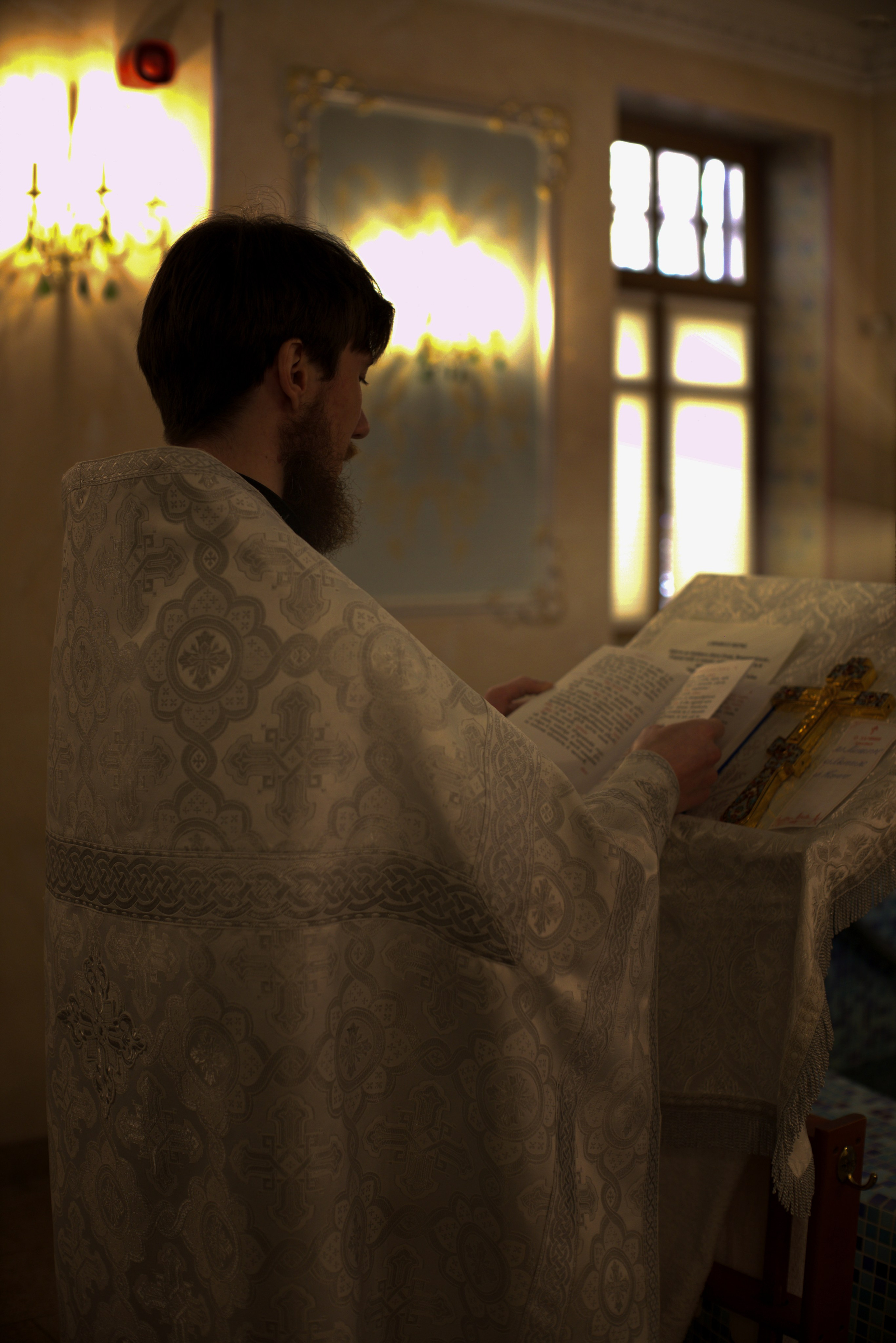 Священник в праздничной ризе читает молитву во время таинства крещения ребенка в храме"