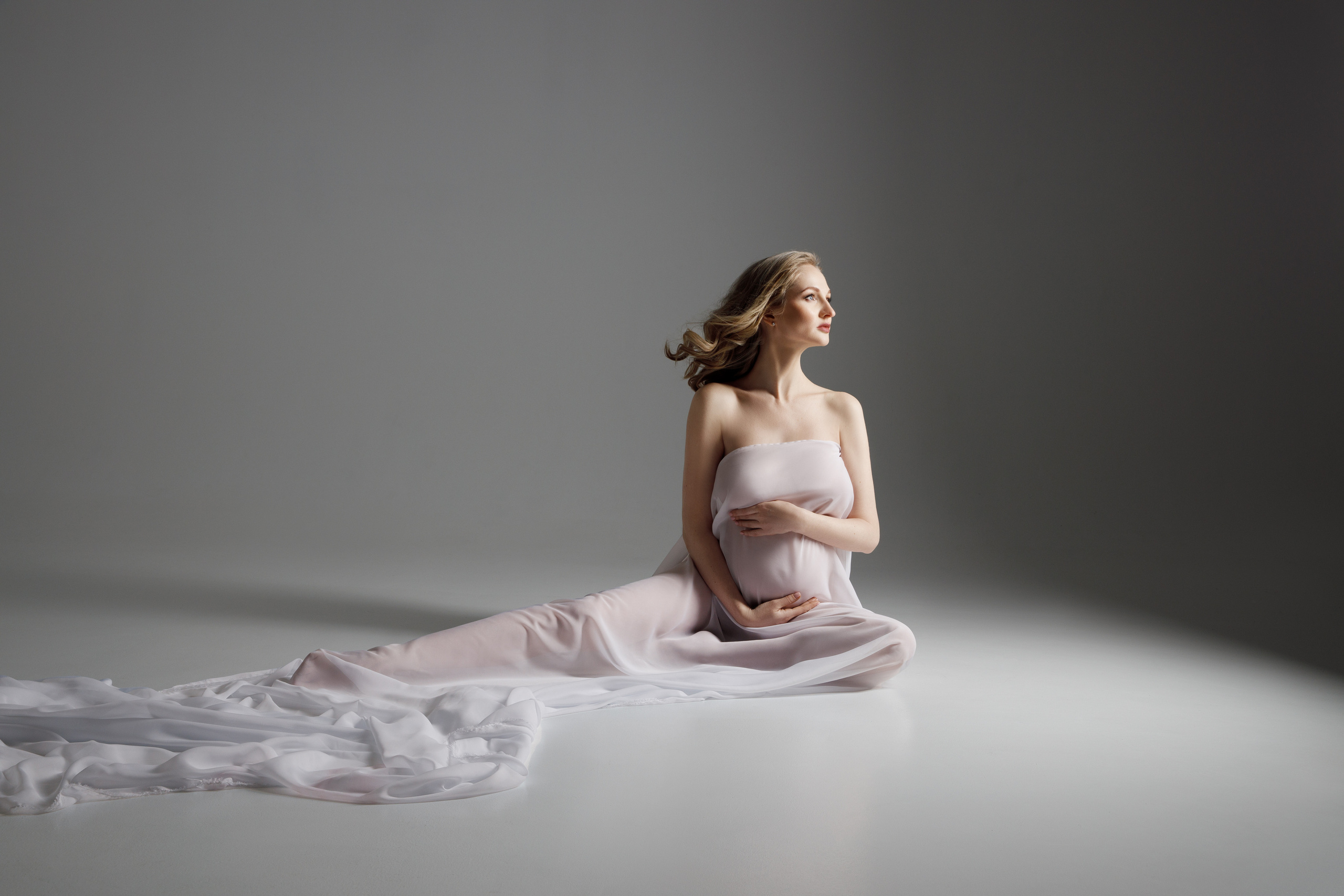 Беременная девушка в прозрачной белой ткани.