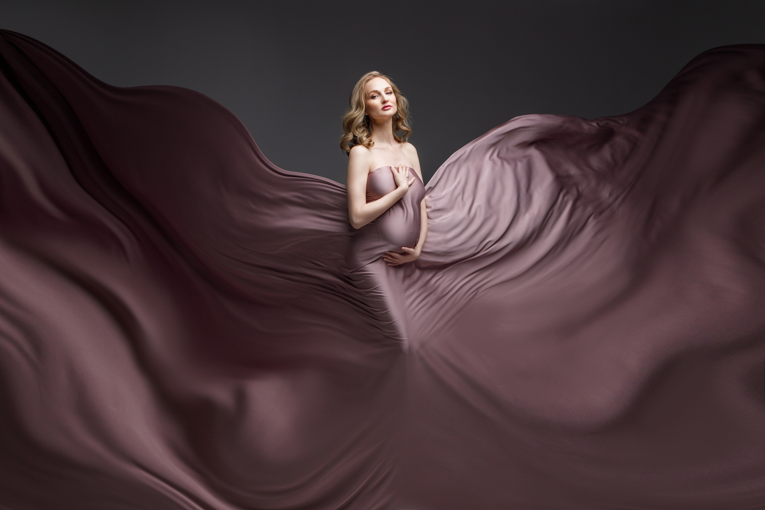 Беременная девушка фотографируется в тканях на фоне.