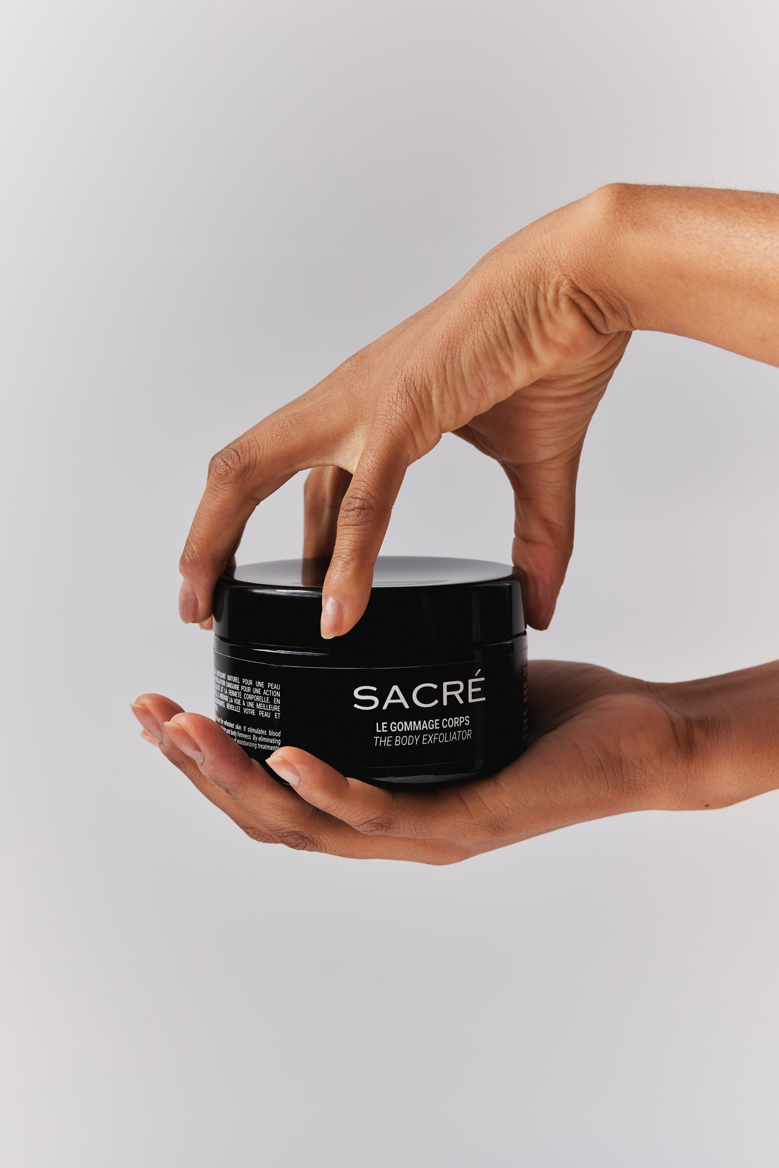 Hand scooping coffee scrub from a jar, showcasing natural skincare product texture.