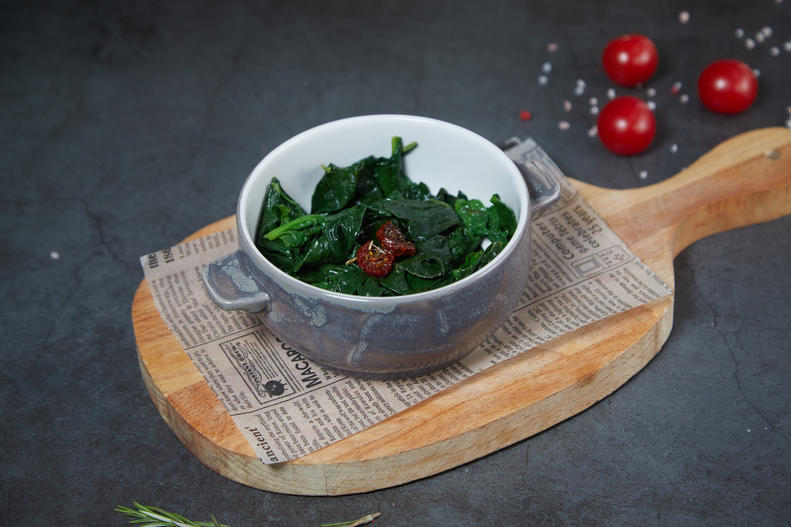 Тёплый шпинат в керамической пиале на деревянной доске.