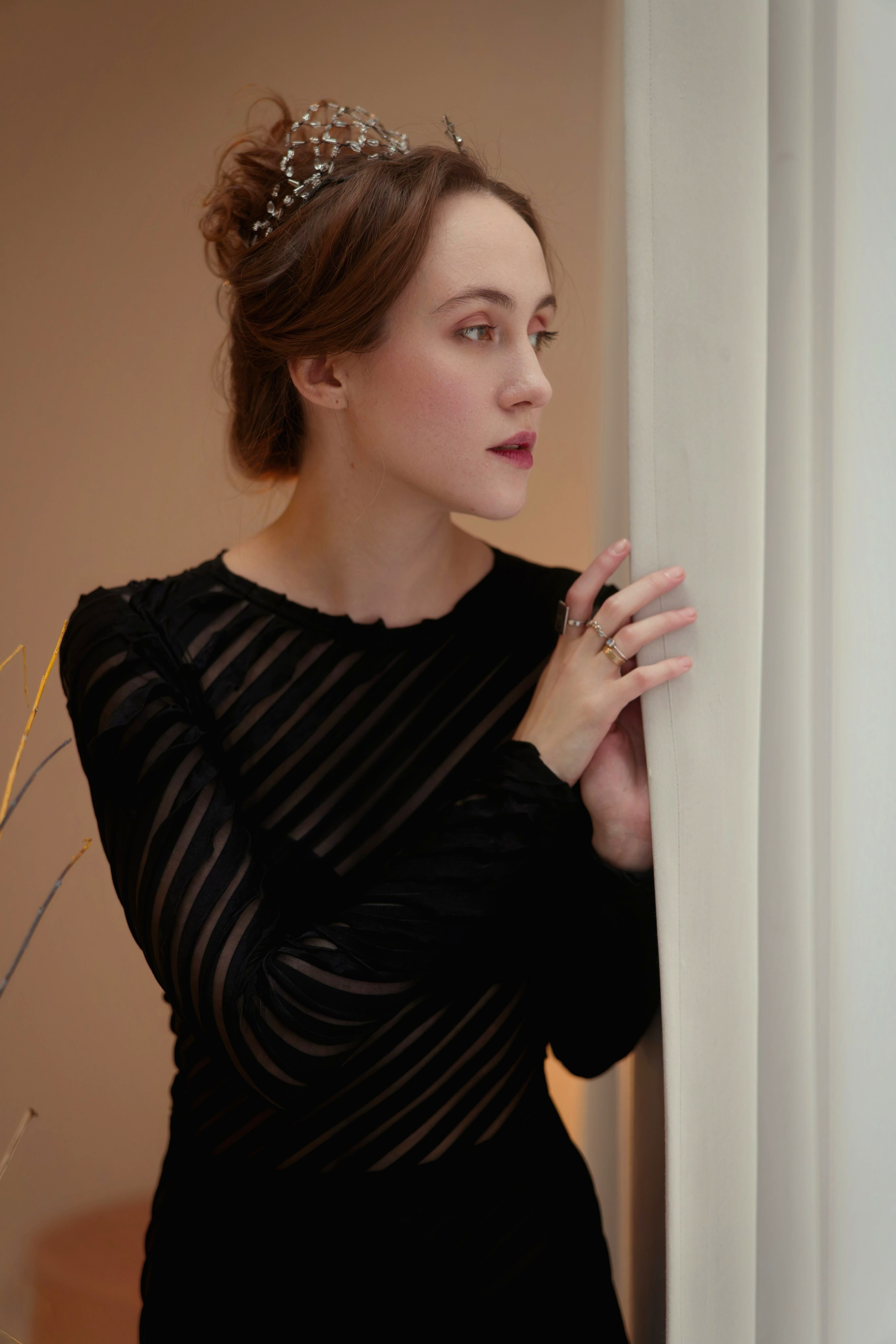 Элегантный портрет девушки с тиарой в черном платье с прозрачными рукавами, профиль у белой колонны, королевский образ