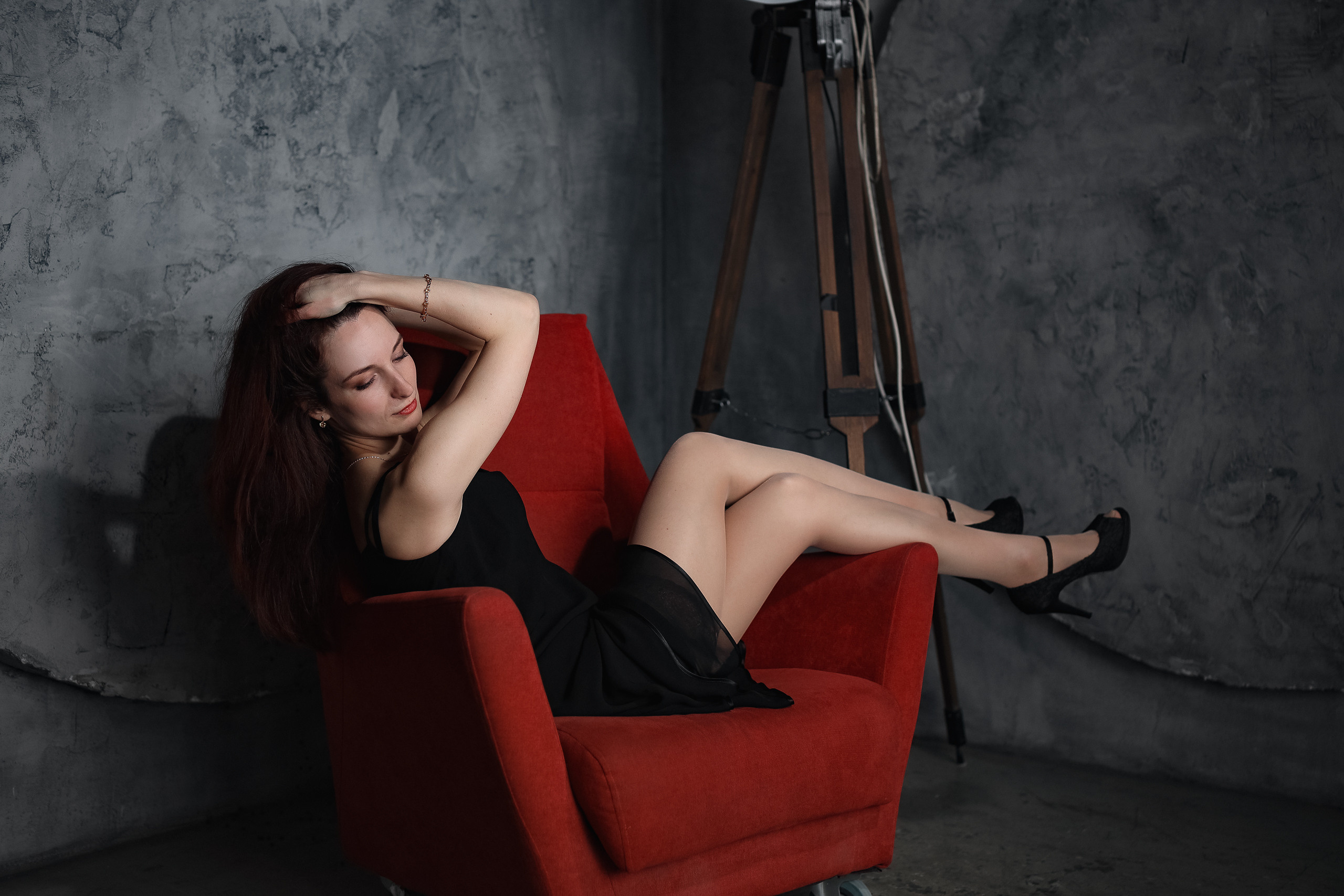 Девушка позирует на красном кресле в студии на портретной фотосессии