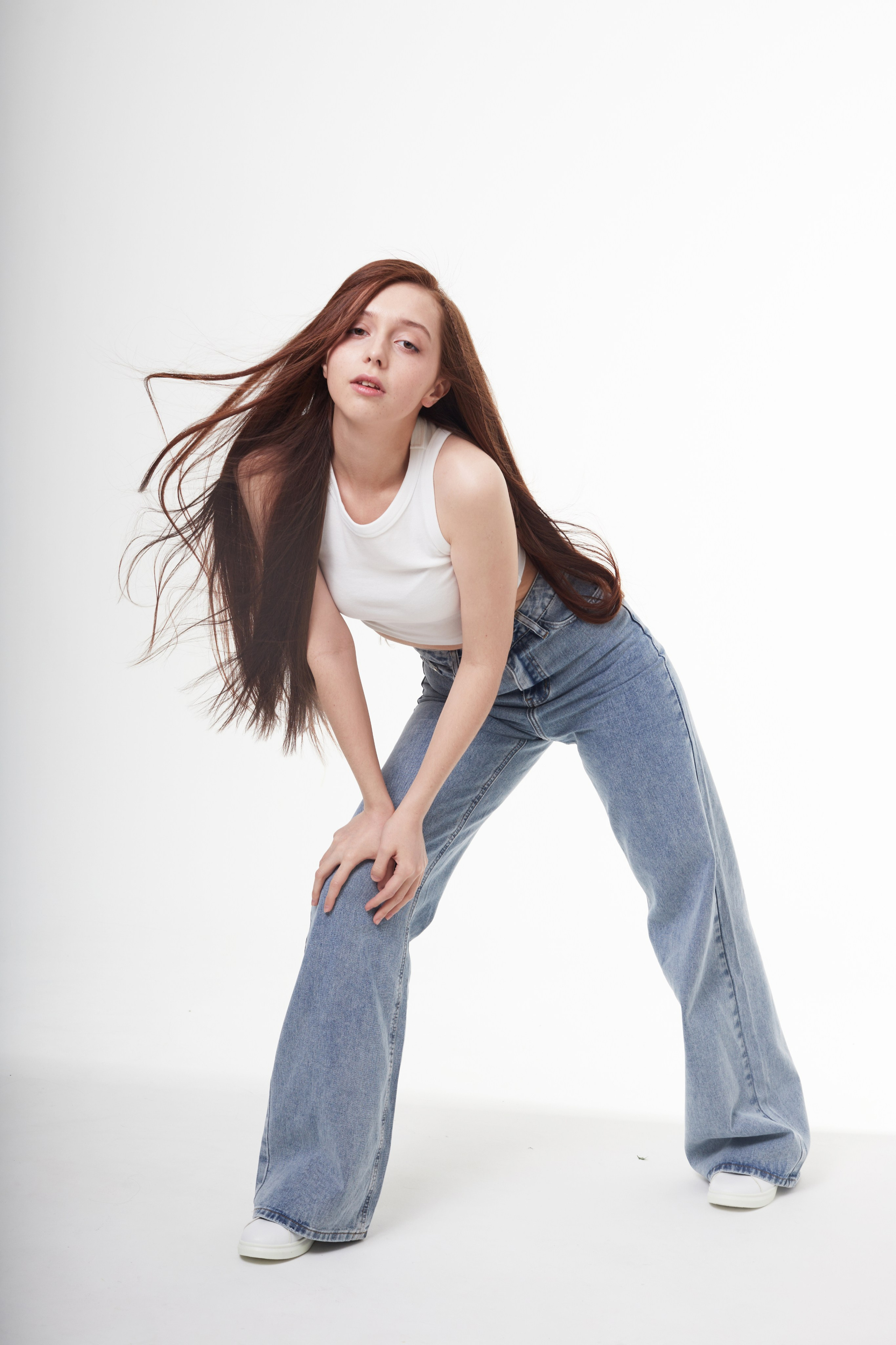 Студийная фотосъёмка девушки с каштановыми волосами в джинсах.