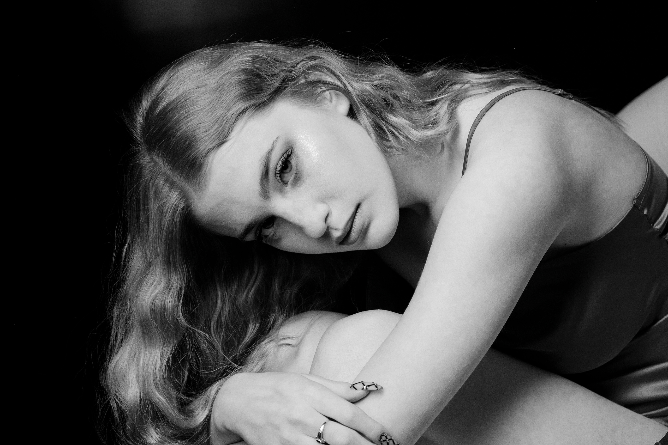 Девушка со светлыми волосами сидит в кресле,склонив голову к коленям и глядя в камеру..