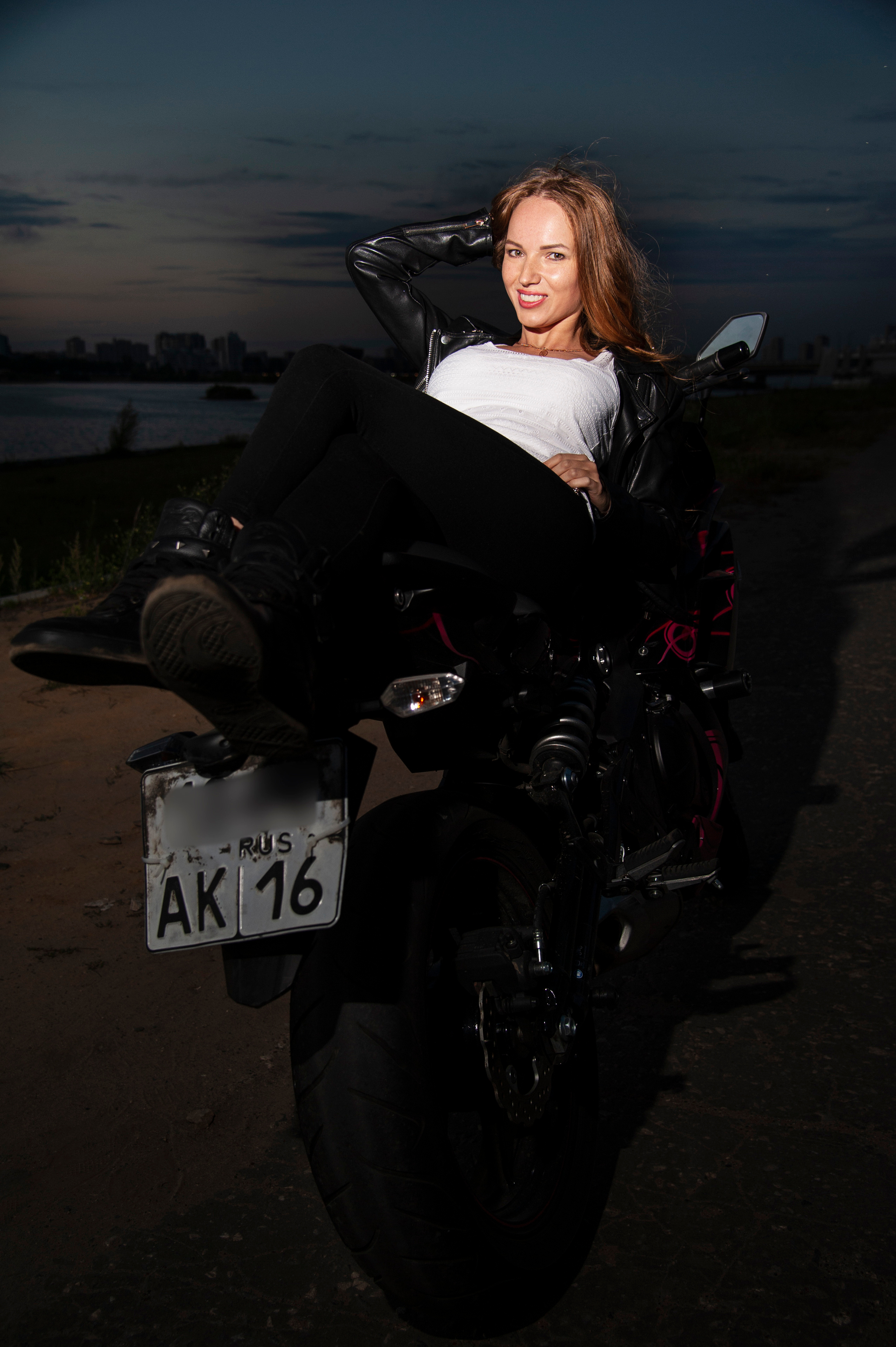 Девушка байкер на своем байке полулежа на закате.