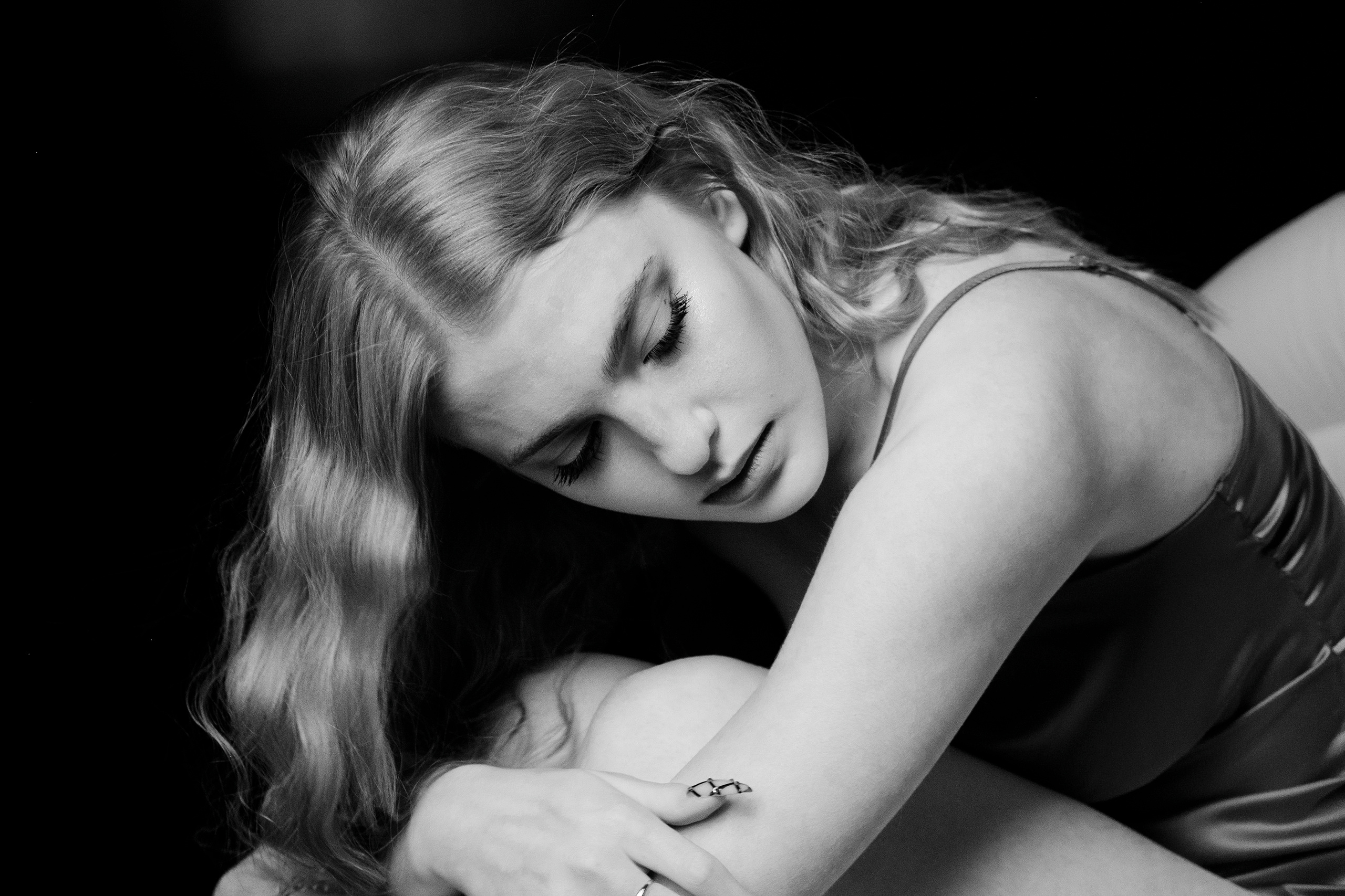 Девушка со светлыми волосами сидит в кресле,склонив голову к коленям и глядя в сторону от камеры...