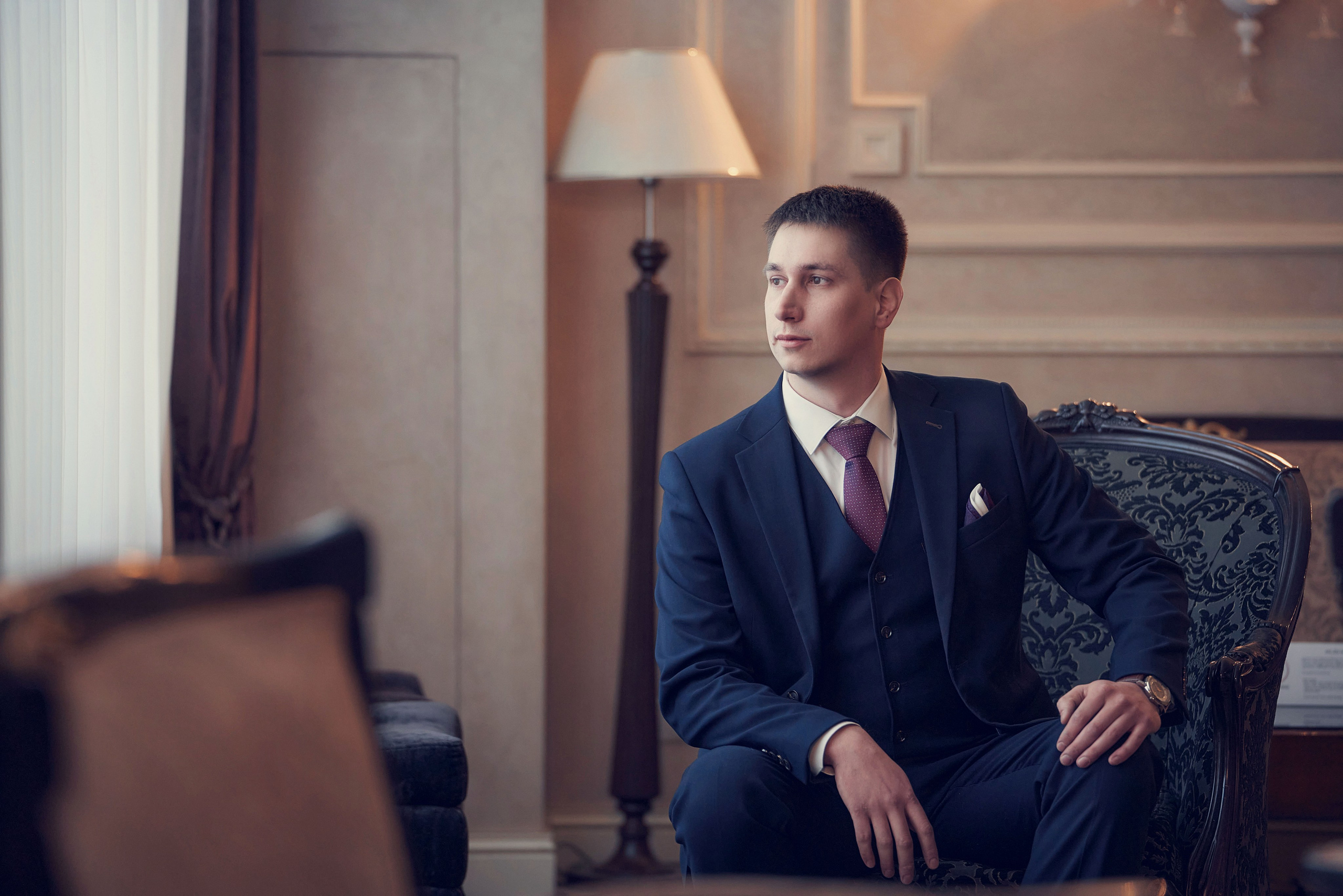 портрет жениха в холле отеля Милан - мужчина сидит в кресле у окна отеля