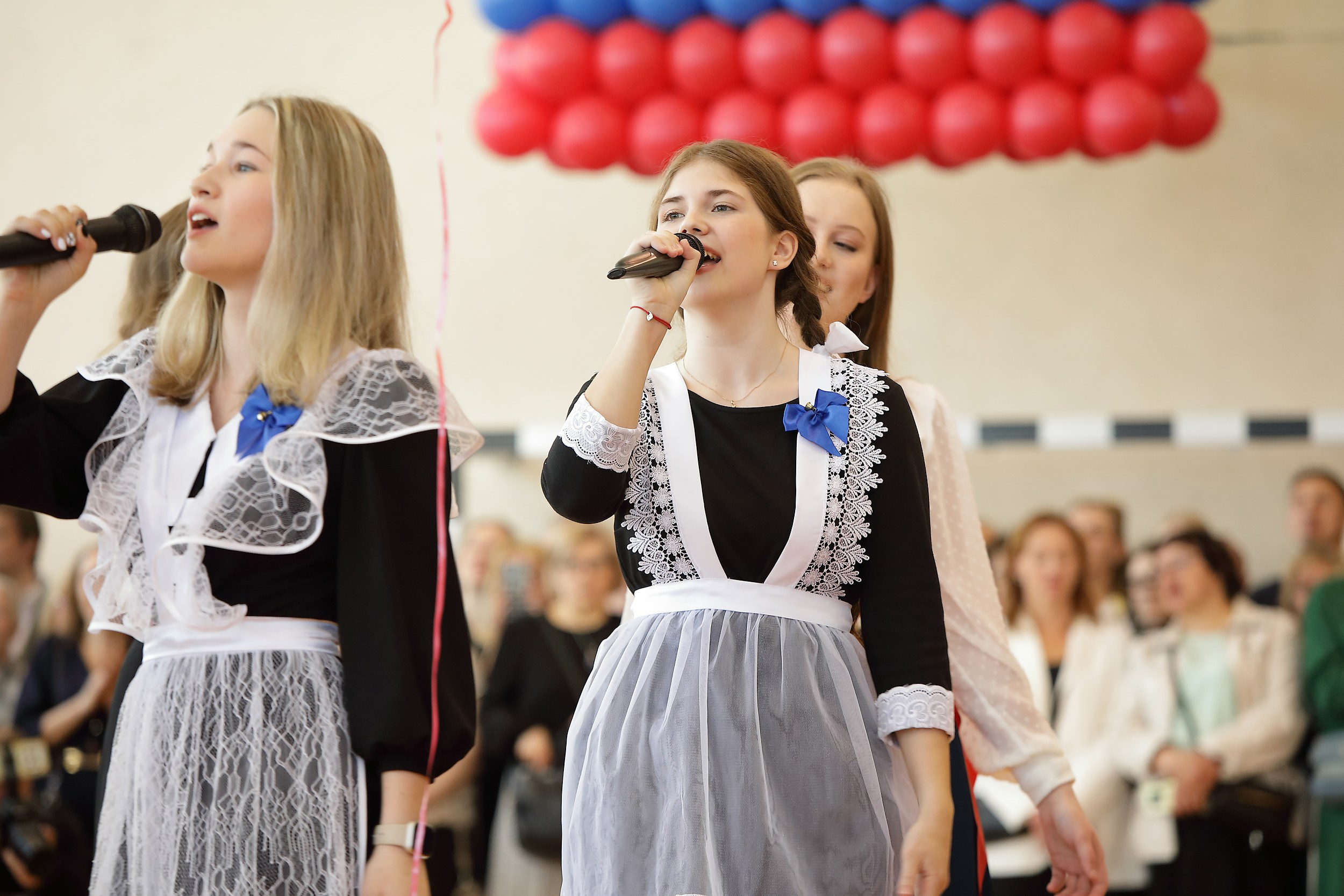 выпускницы в черных платьях с белыми фартуками