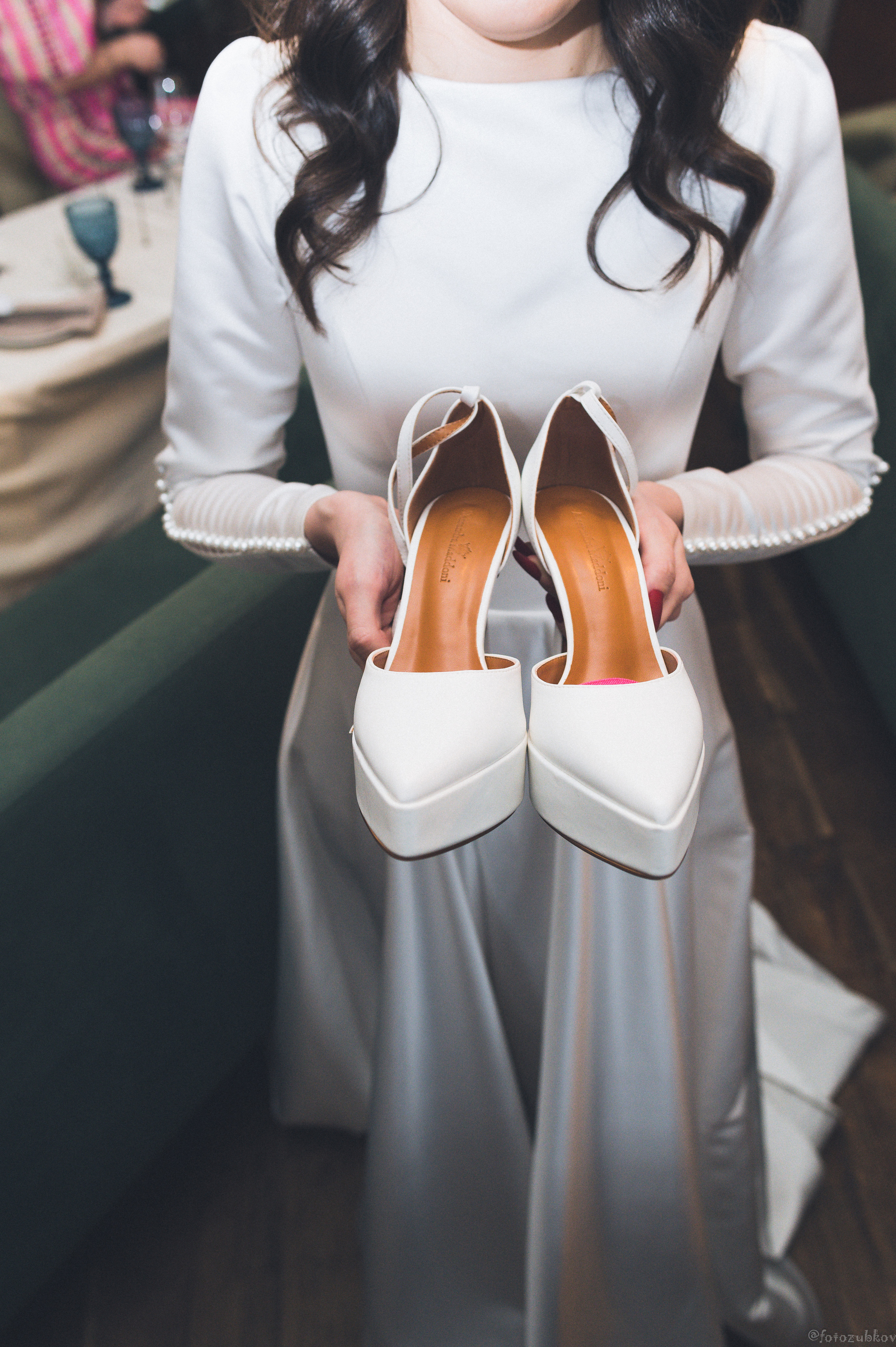 Невеста в белом платье держит свои туфли