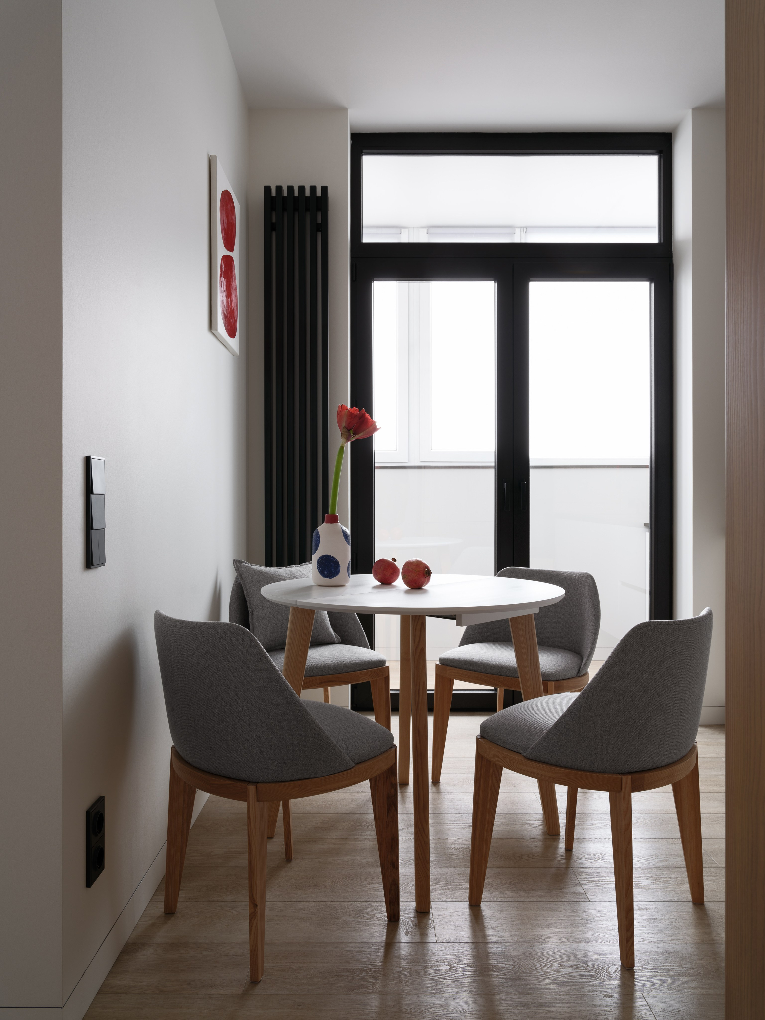 Кухня-столовая в современном стиле с круглым белым столом, мягкими серыми стульями и декором в красных акцентах. Дизайн интерьера от Евгении Княжевой и Владлены Приваловой, фото Сергея Денисенко