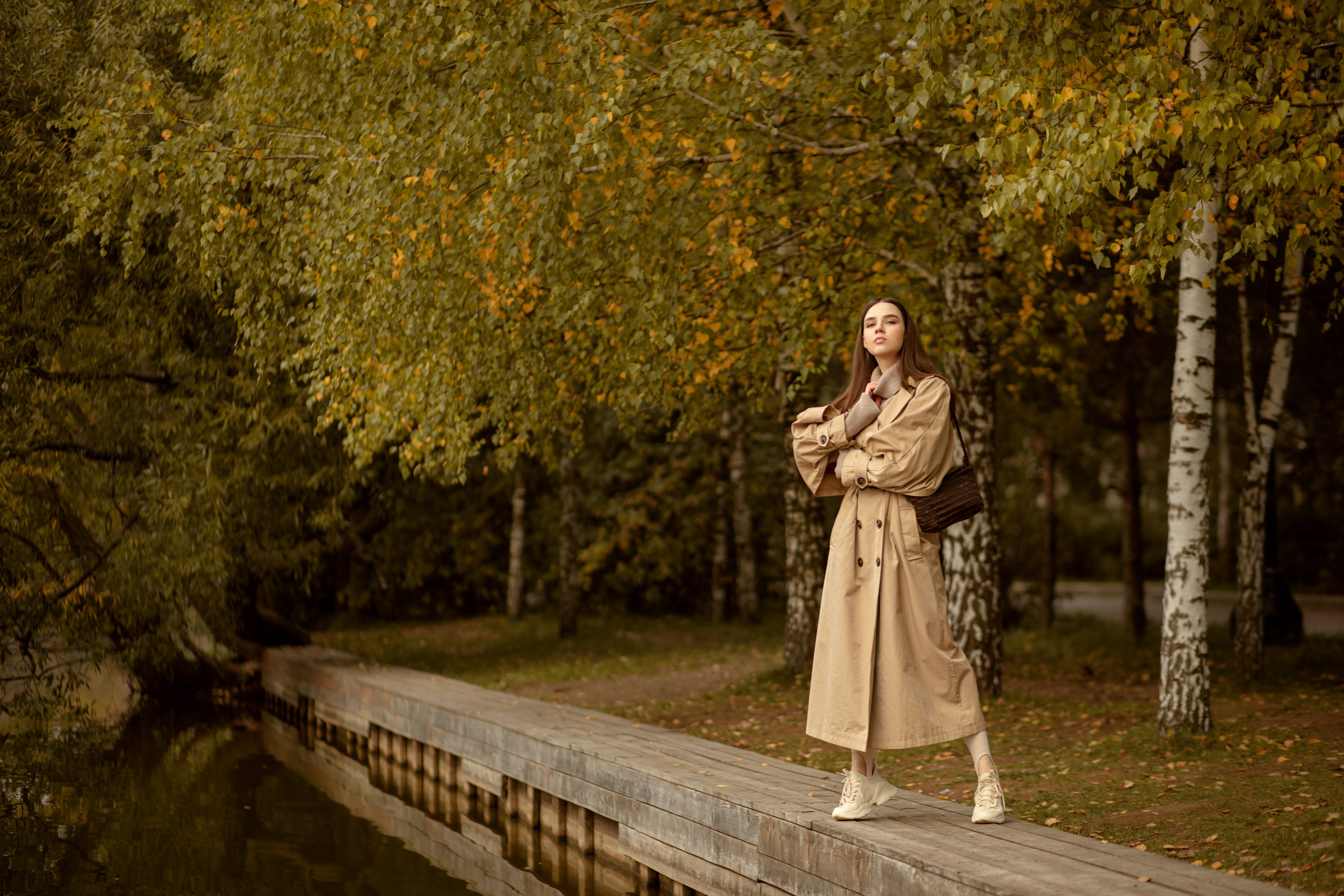 Девушка в коричневом тренче любуется осенним парком