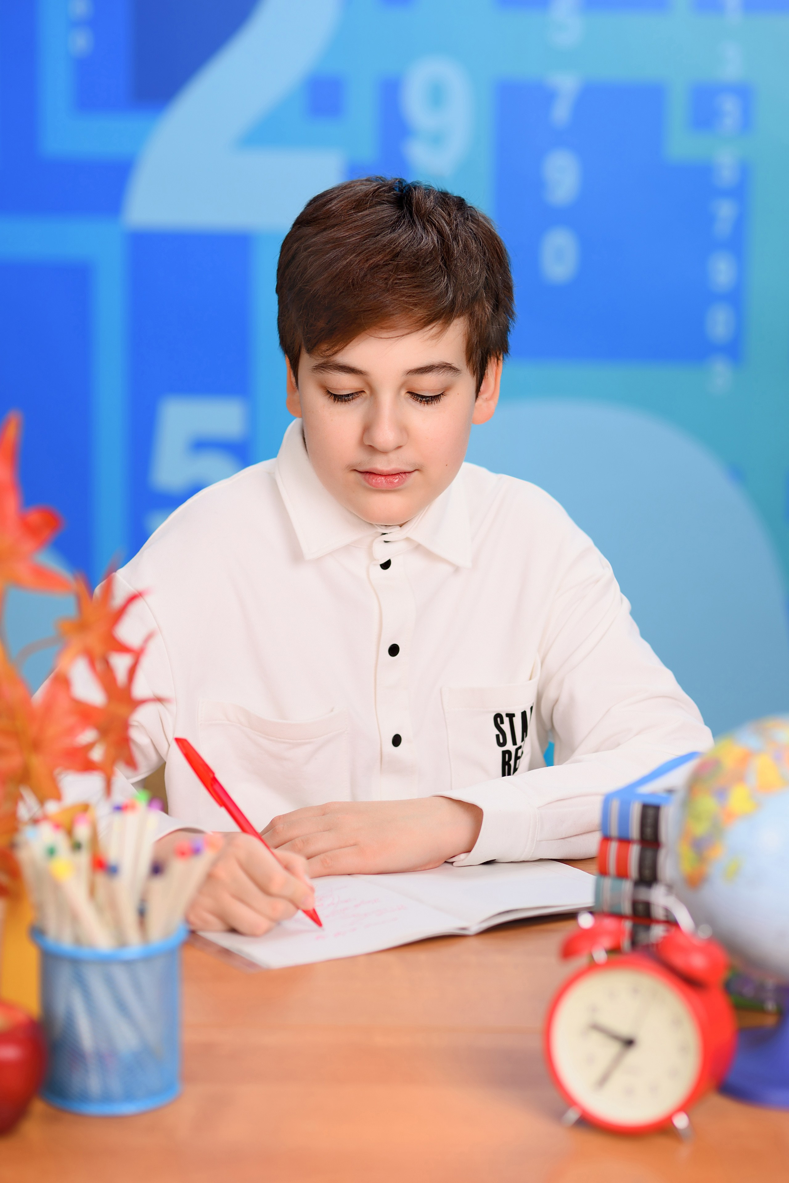 Портрет школьника за школьной партой, держащего шариковую ручку и пишущего в тетради.