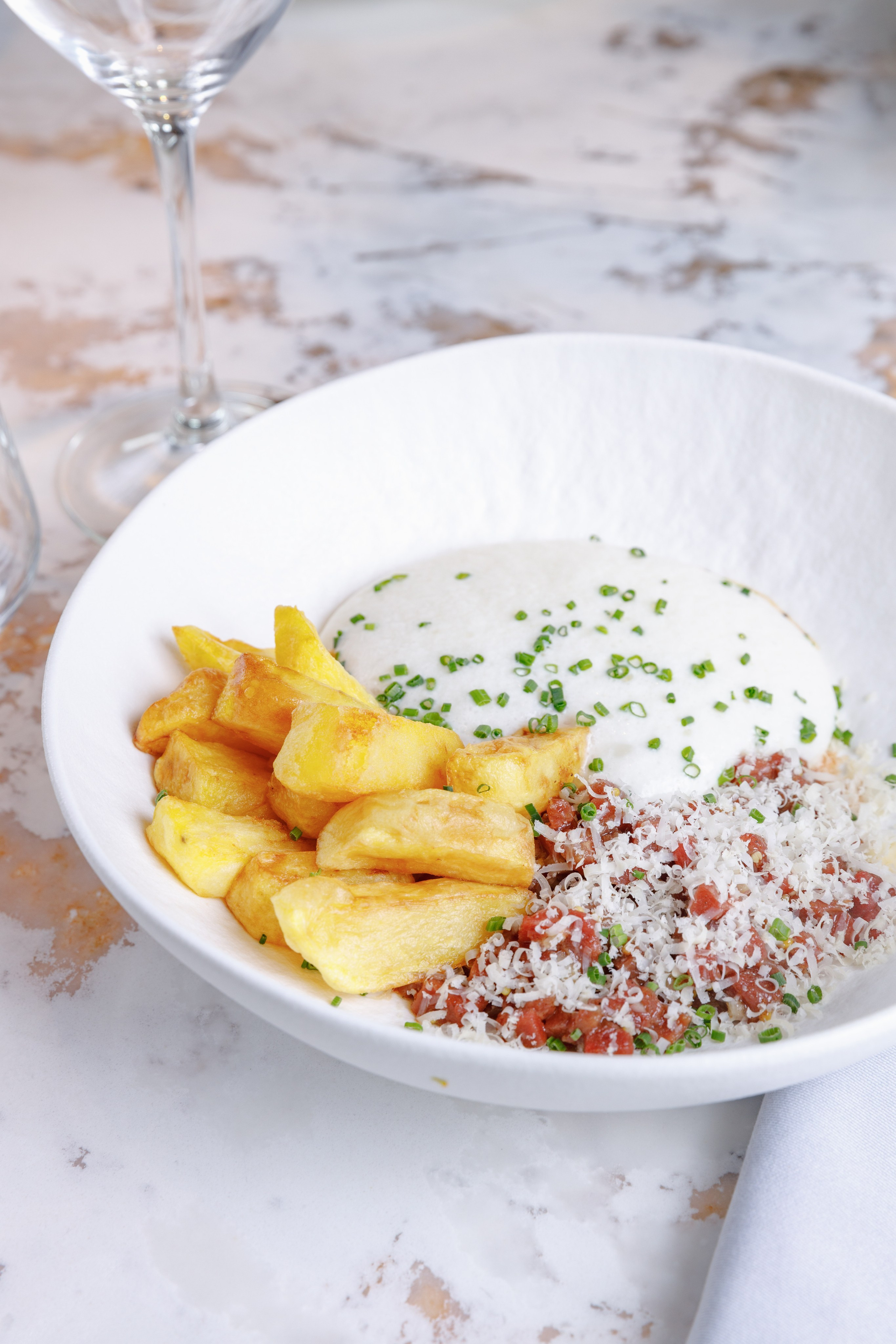 Ресторанная подача мясной закуски с золотистыми картофельными дольками на светлом мраморном столе у бокала