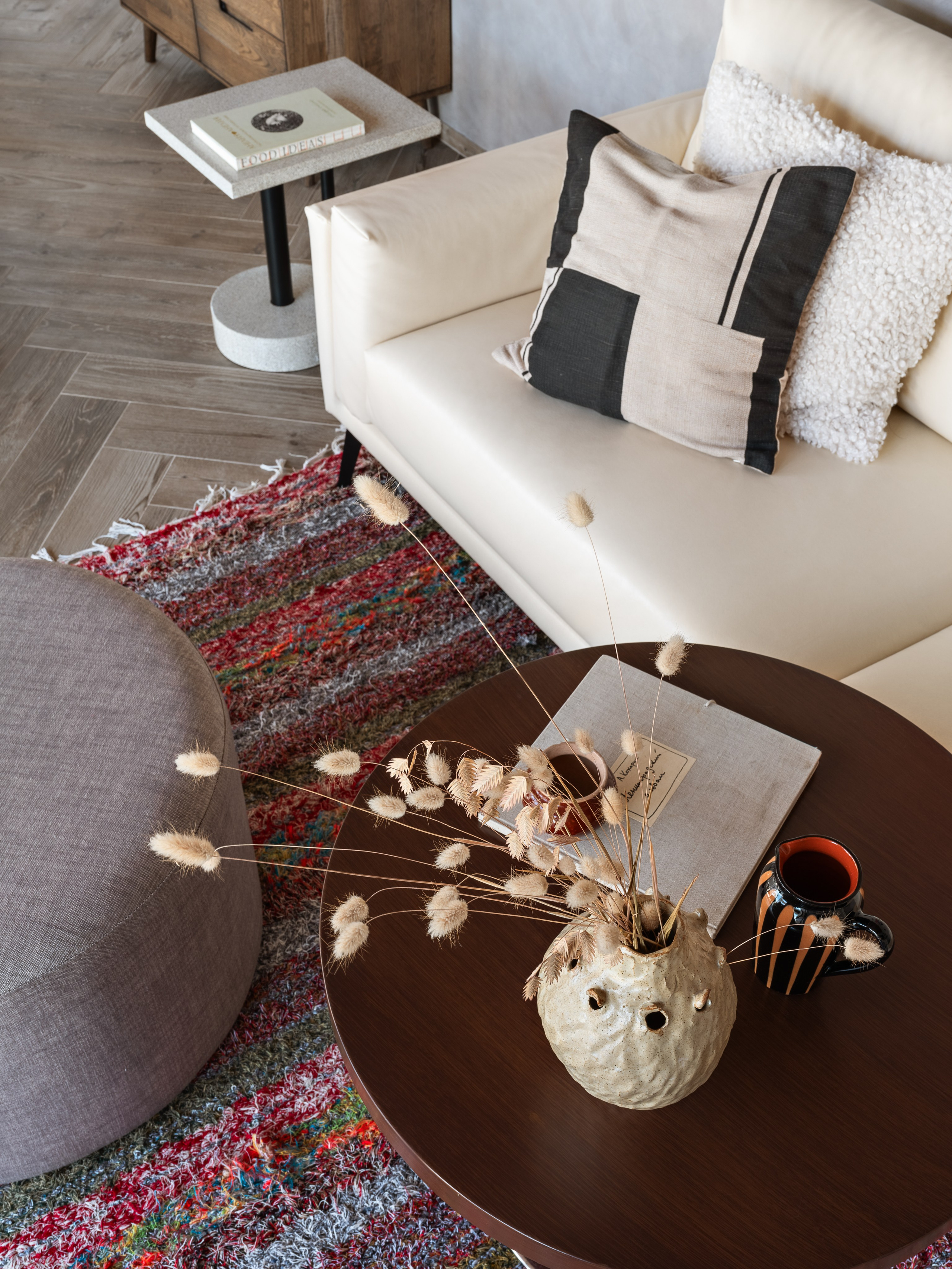 Круглый журнальный столик в гостиной с керамической вазой и сухоцветами, на фоне белого дивана и ковра с ярким рисунком; интерьер от Наталии Шелепниковой, стилист София Калбазова, фотограф Сергей Денисенко.