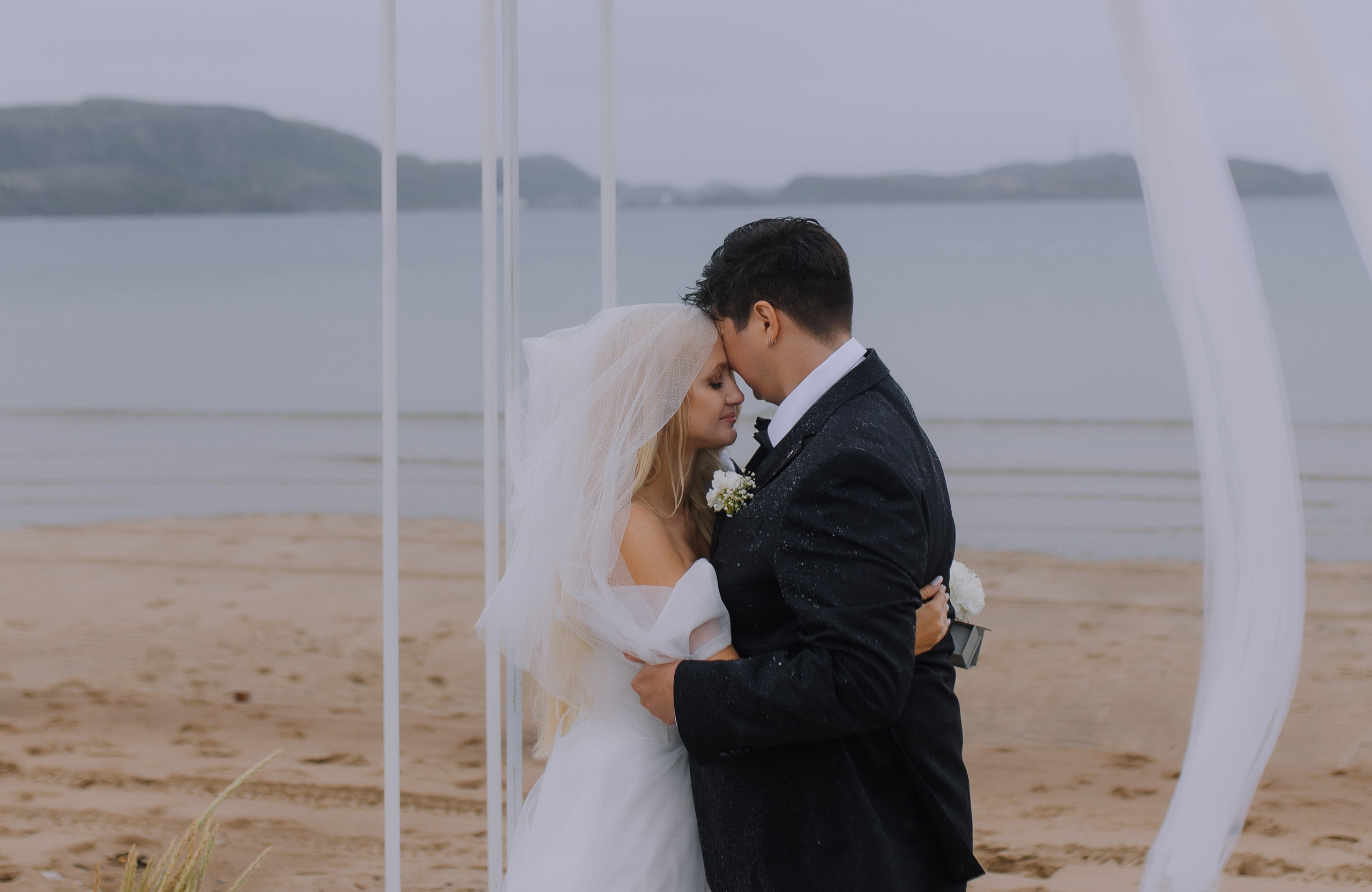 Невеста в белом платье идёт босиком по каменистому пляжу Териберки.