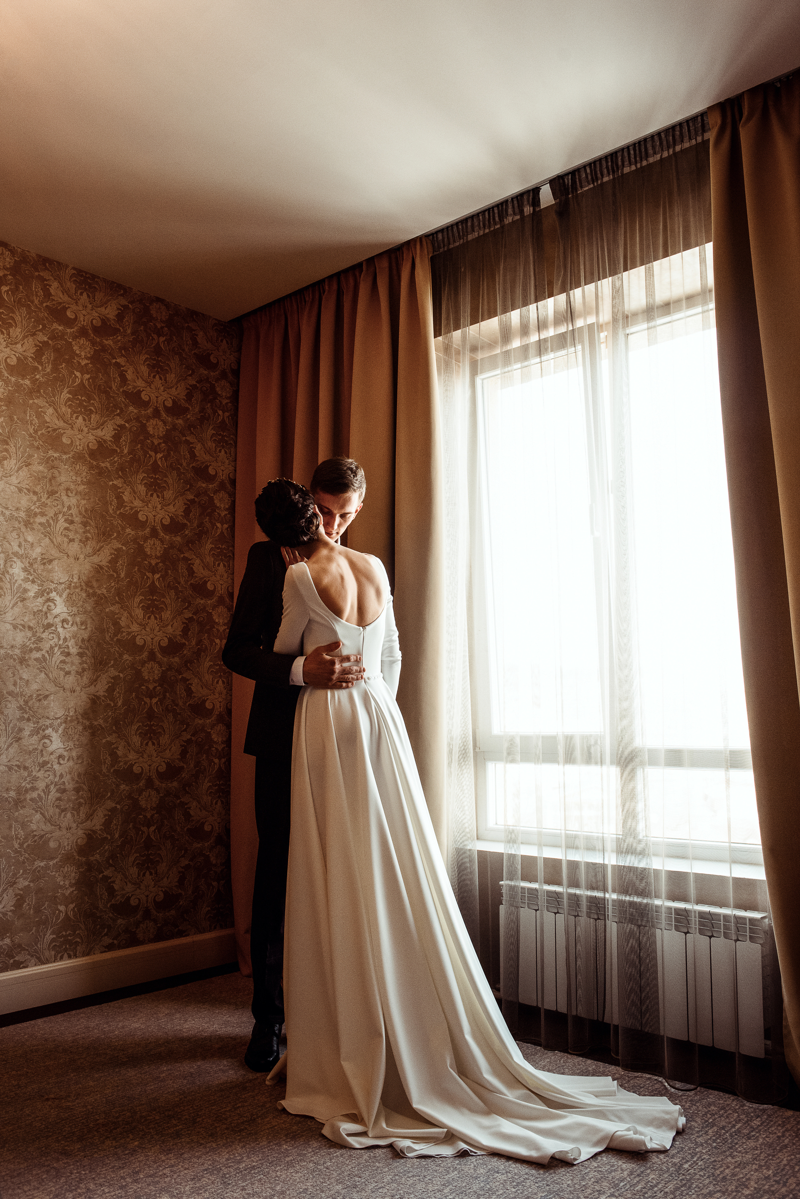 Молодожёны стоят у окна в комнате с классическим интерьером 
