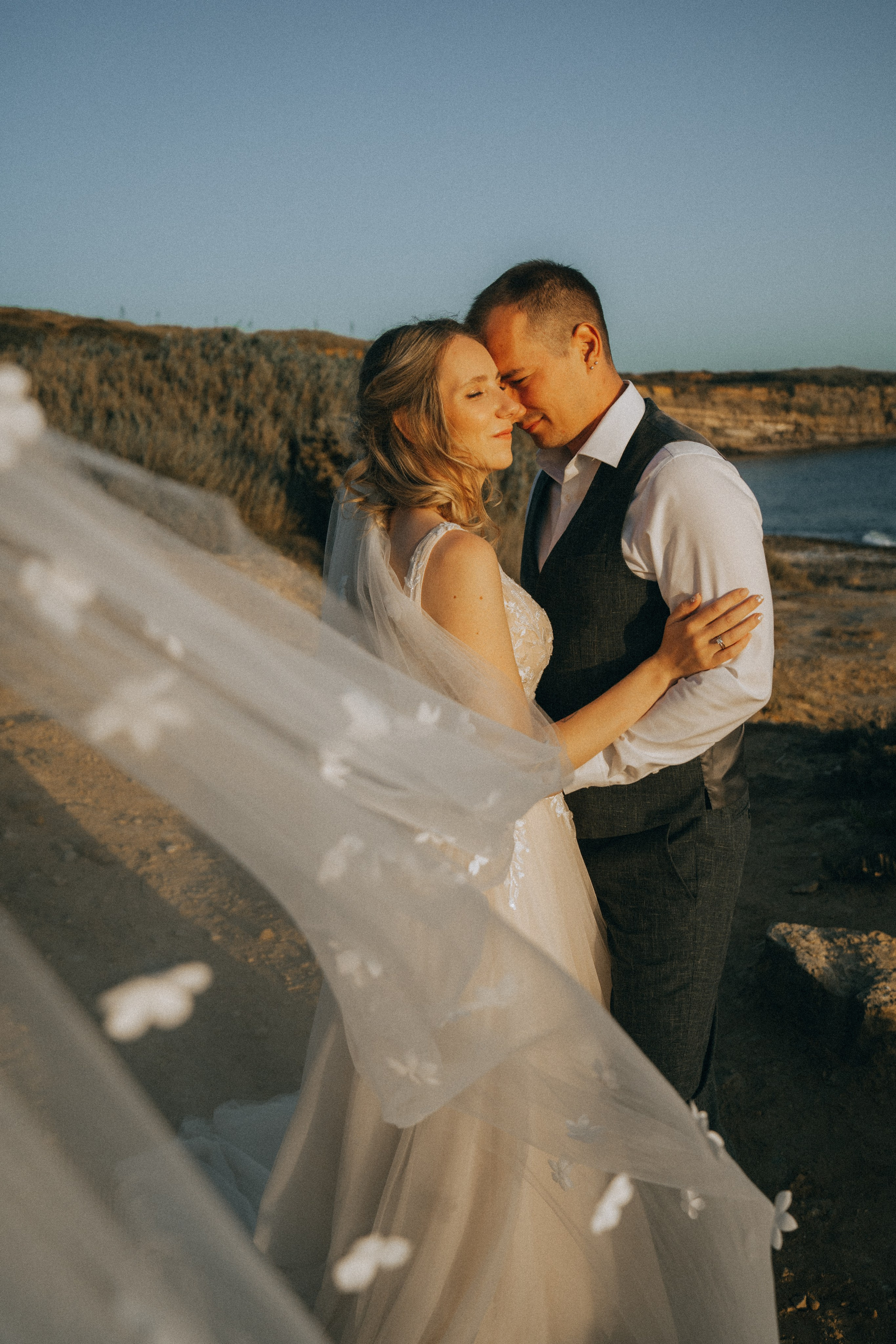 Счастливая пара жених и невеста целуется на фоне волн  скал и заката у океана.