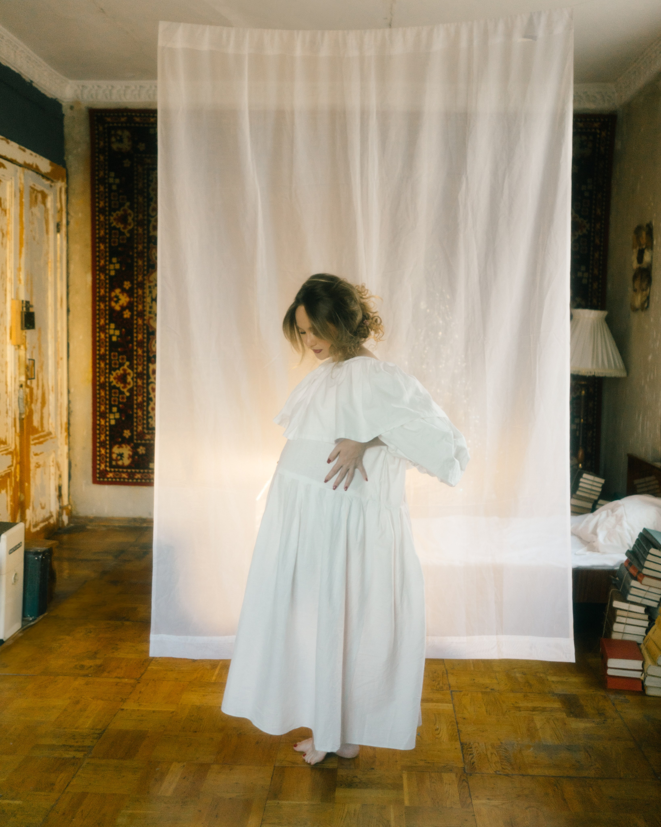 Полный рост: беременная в длинном винтажном белом платье перед полупрозрачной тканью, ретро-интерьер — художественная фотосессия беременности в СПб в киношном стиле. 