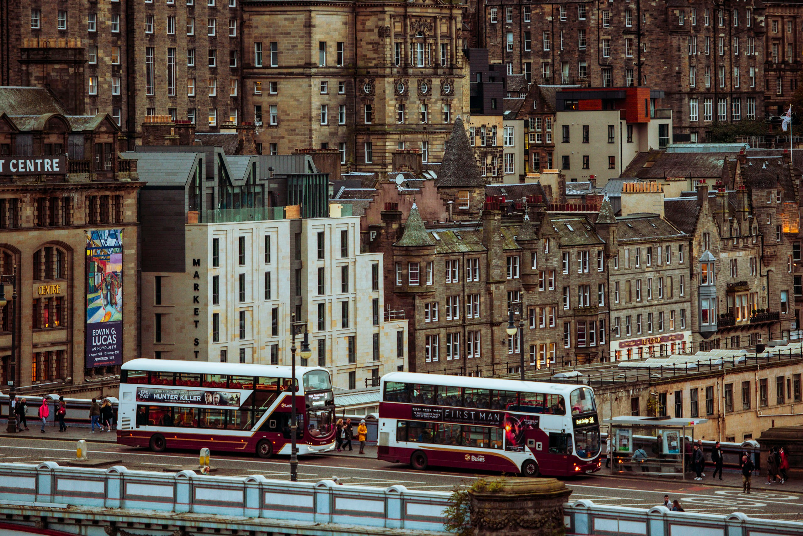 Оживленная улица в центре Эдинбурга, Шотландия, с двумя красными двухэтажными автобусами Lothian Buses и историческими каменными зданиями на заднем плане.