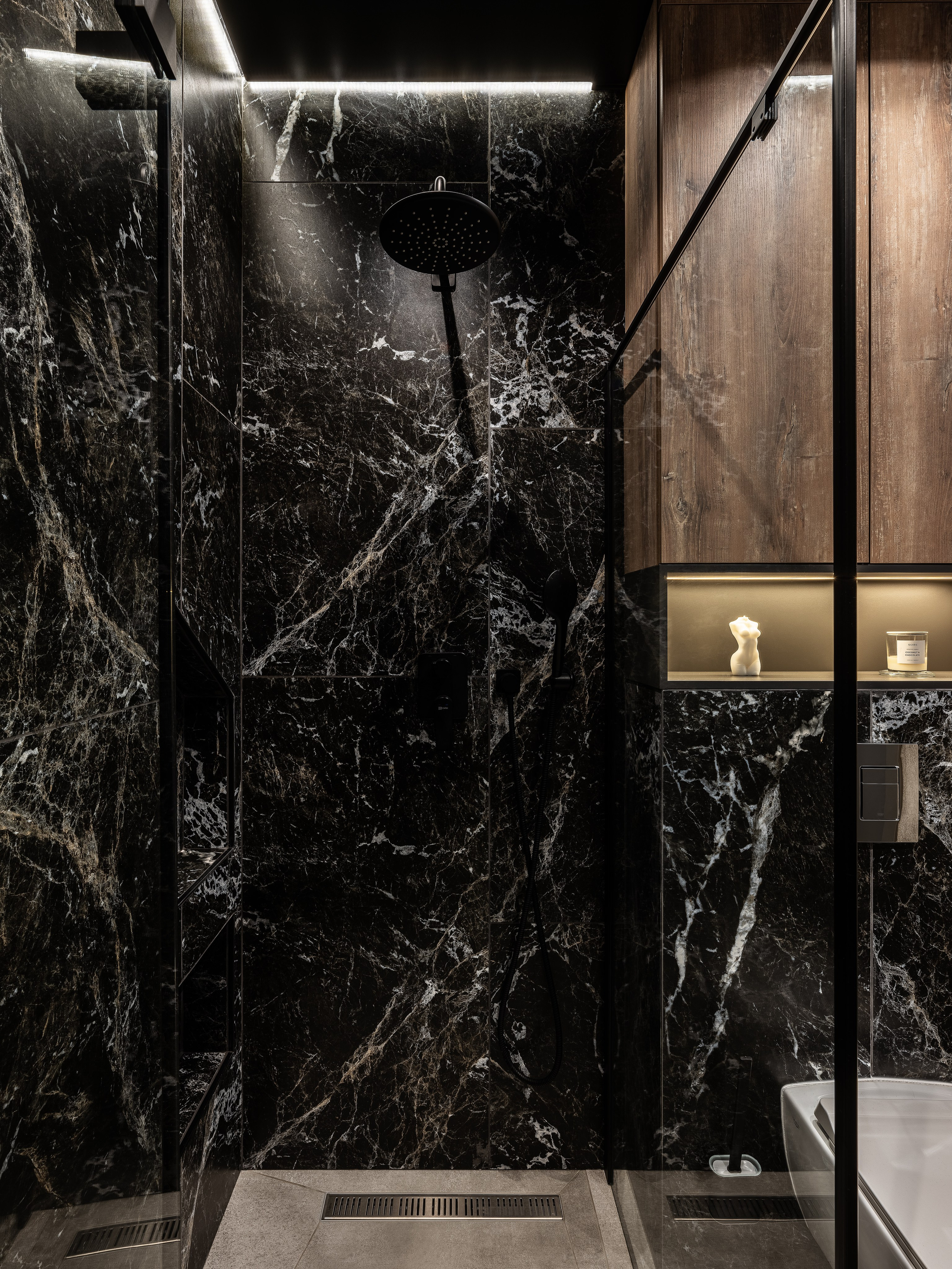Интерьер современной ванной комнаты с душевой кабиной, отделанной черным мрамором с белыми прожилками, встроенной подсветкой и минималистичной сантехникой; проект дизайнер Екатерина Мищенко, фото Сергей Денисенко.
