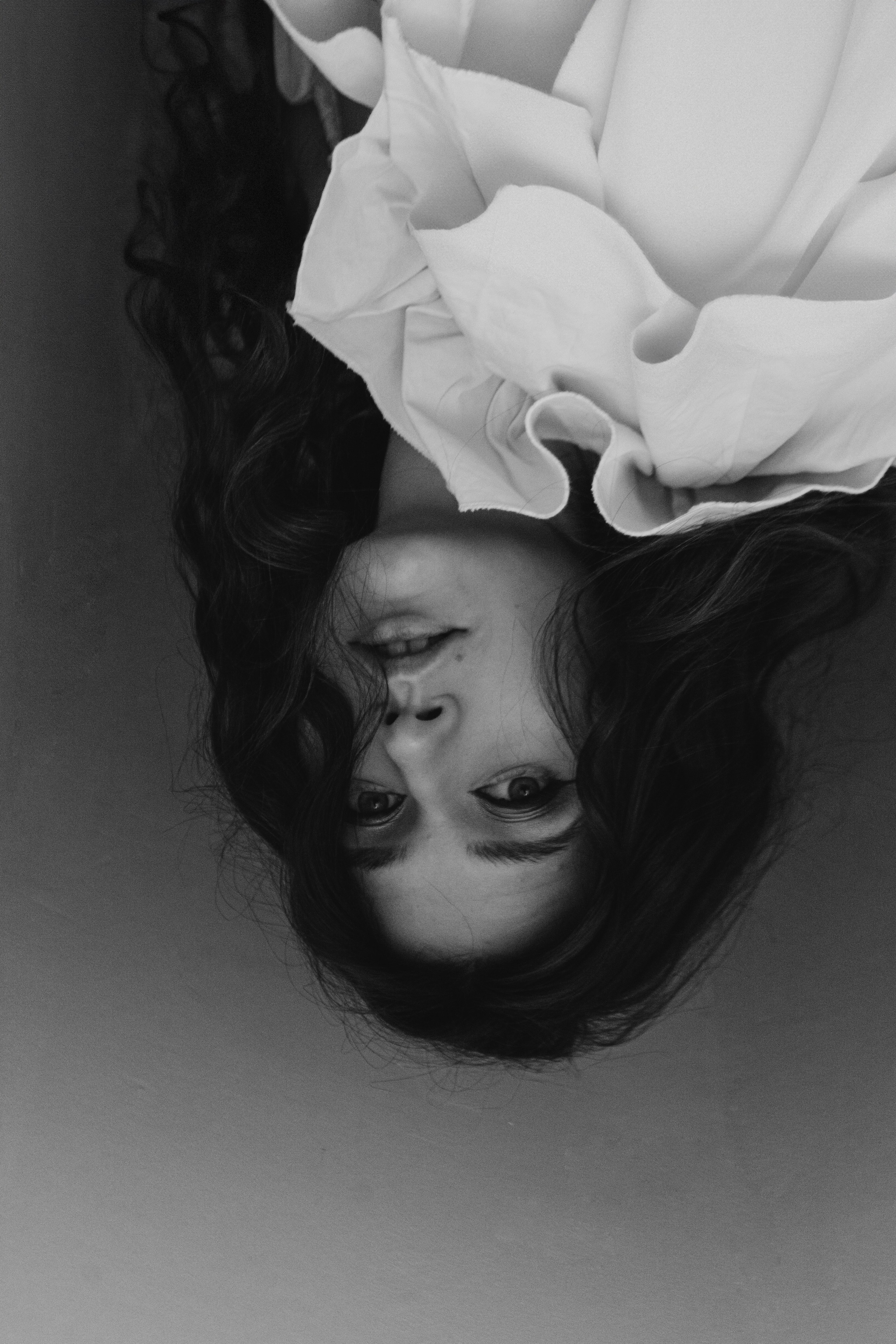 Перевернутый черно-белый потрет девушки на белом фоне. У модели длинные волосы и объемная белая блуза. Она смотрит на нас