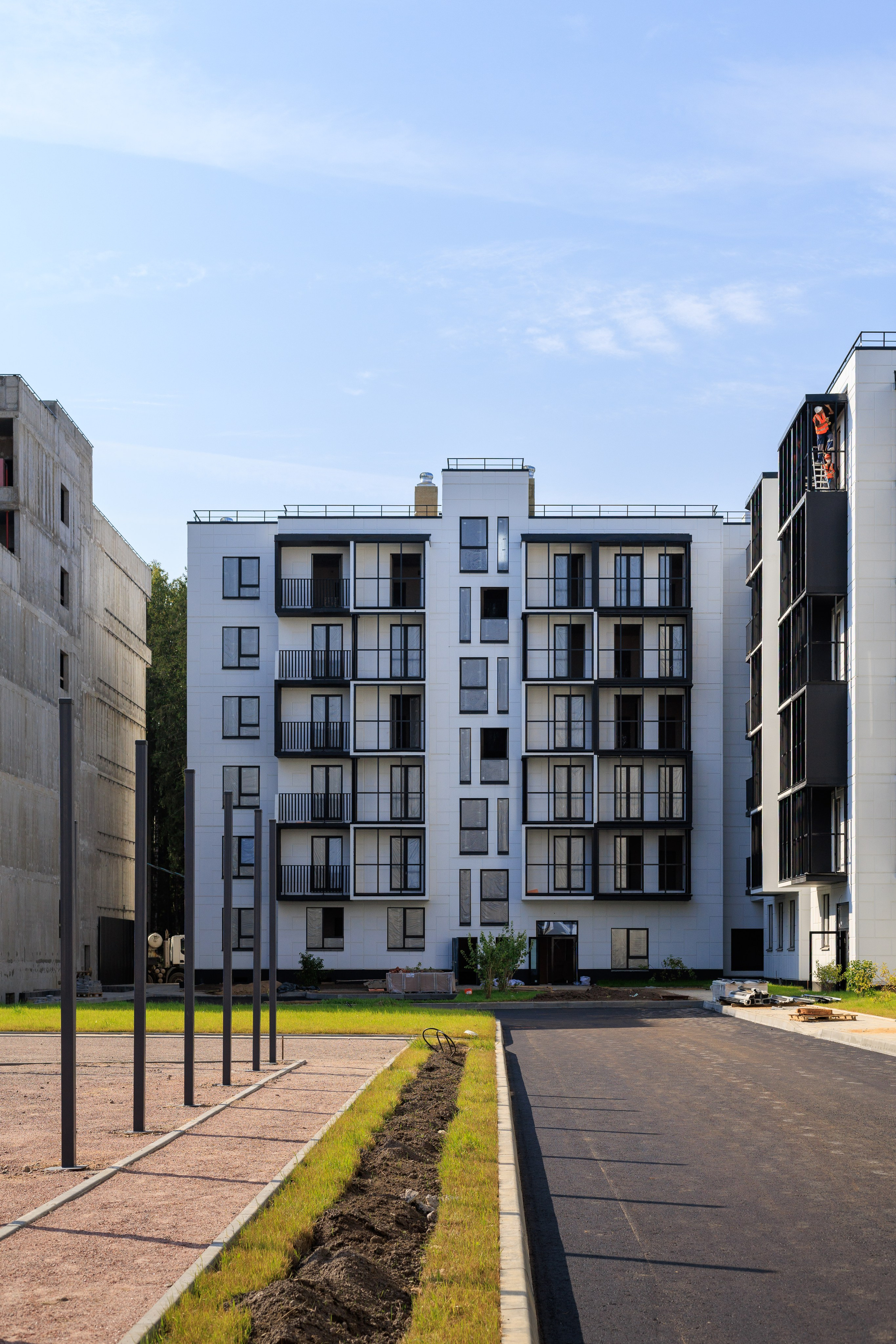 На изображении представлен вид на городские улицы с современными зданиями. Это может быть городской пейзаж, показывающий высотное здание с несколькими рядами окон, возможно, это жилой комплекс или офисное здание.