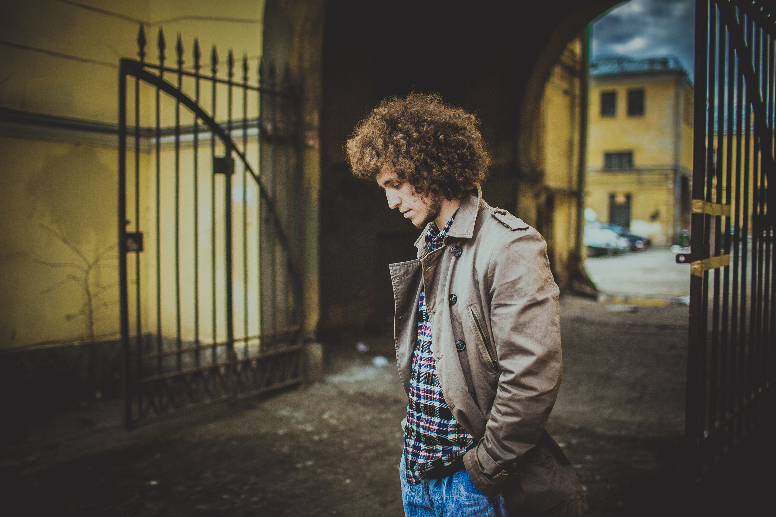 портрет кудрявого юноши в бежевом плаще и клетчатой рубашке