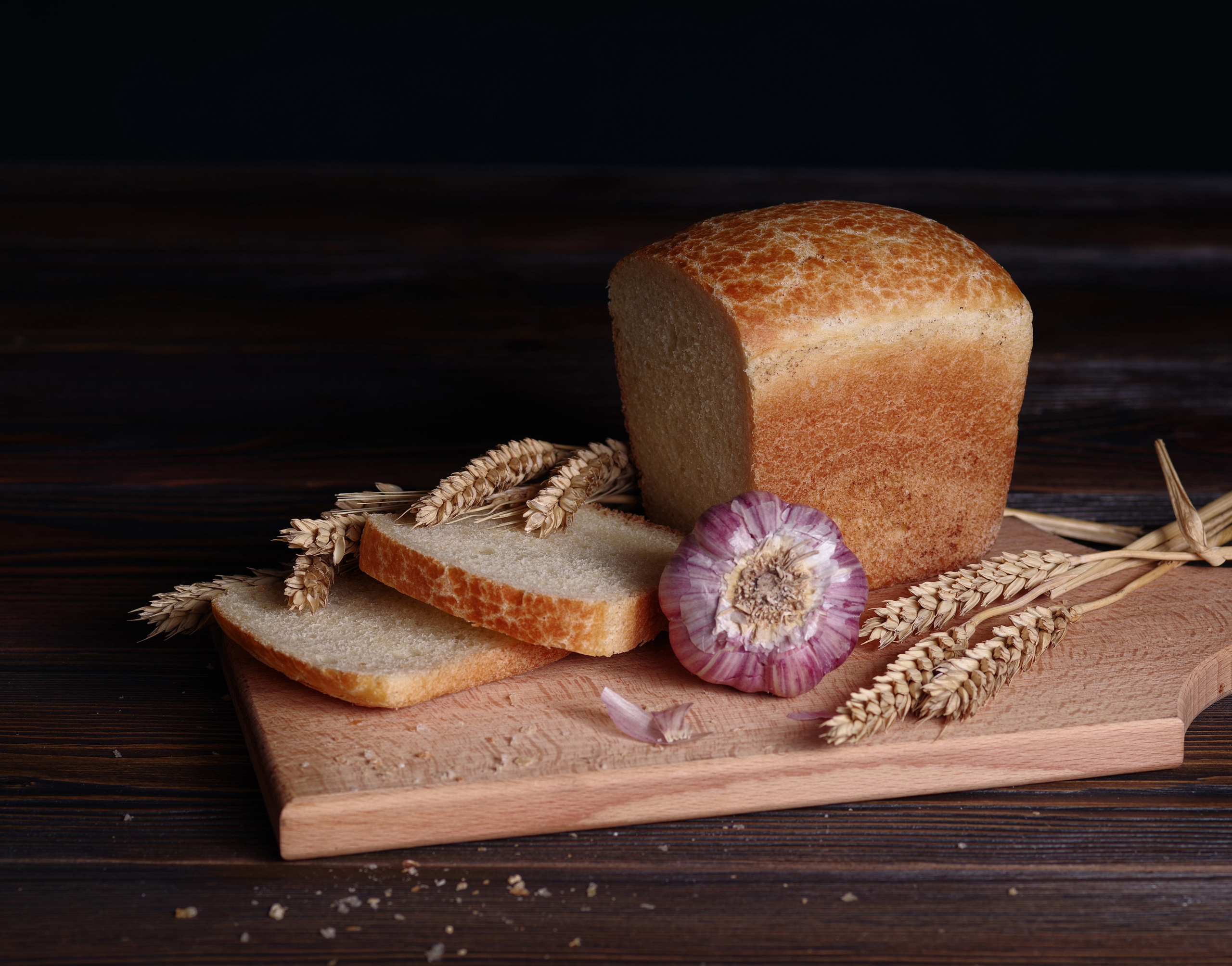 Буханка хлеба с нарезанными ломтиками и чесноком с колосьями пшеницы