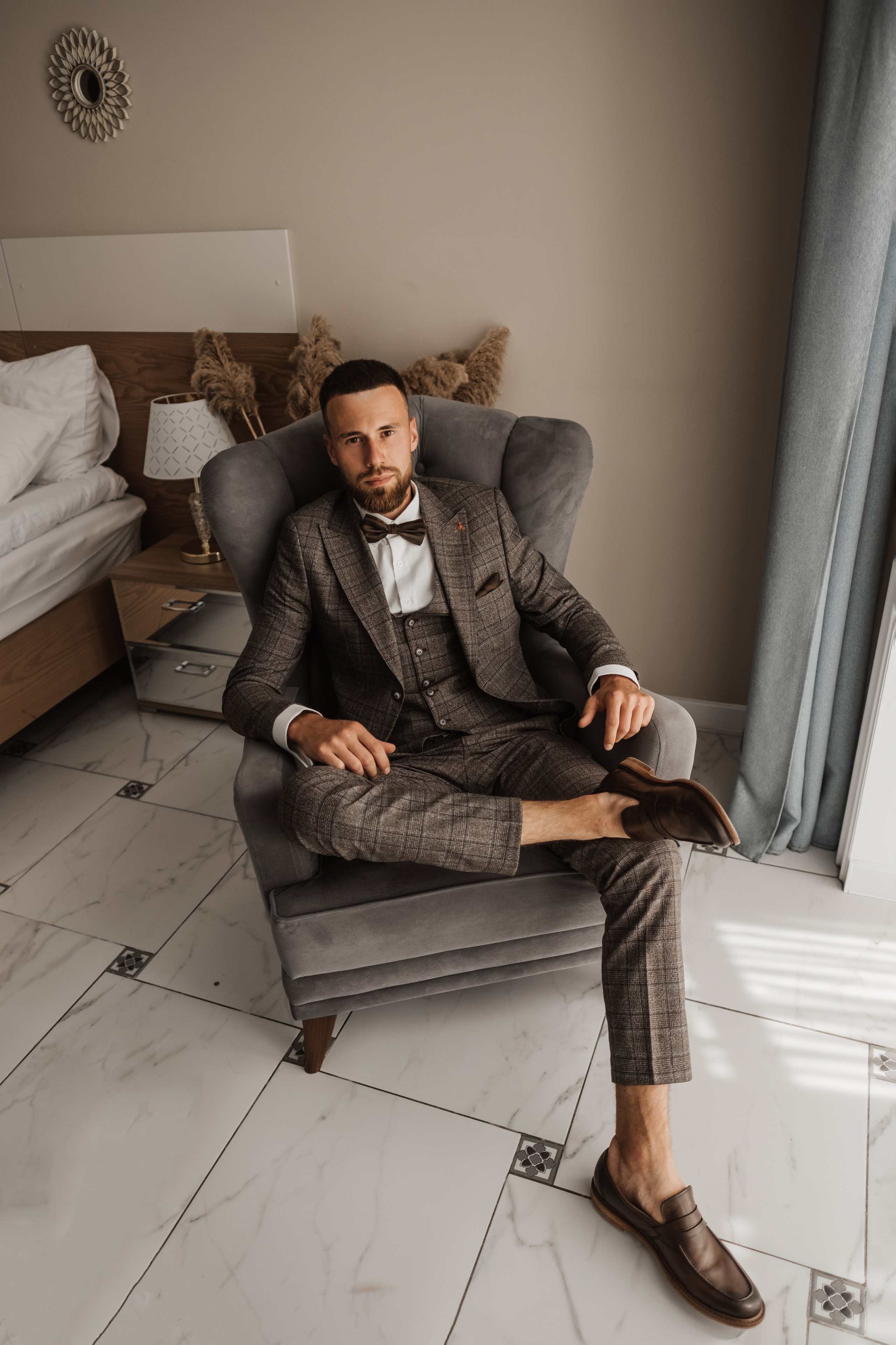 Мужчина в пиджаке, белой рубашке и бабочке сидит на кресле.