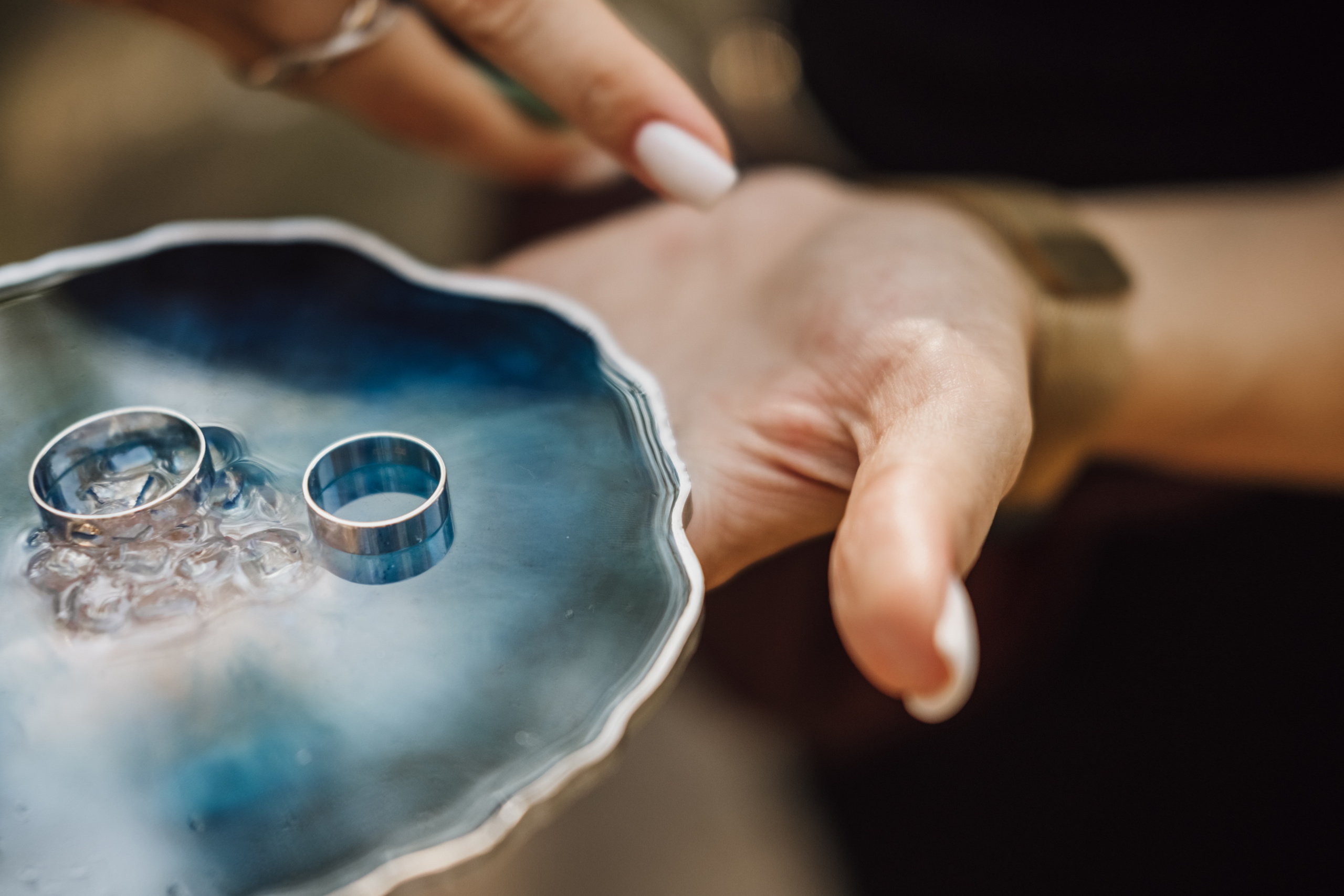 Рука держит обручальные кольца на специальной подставке для колец.