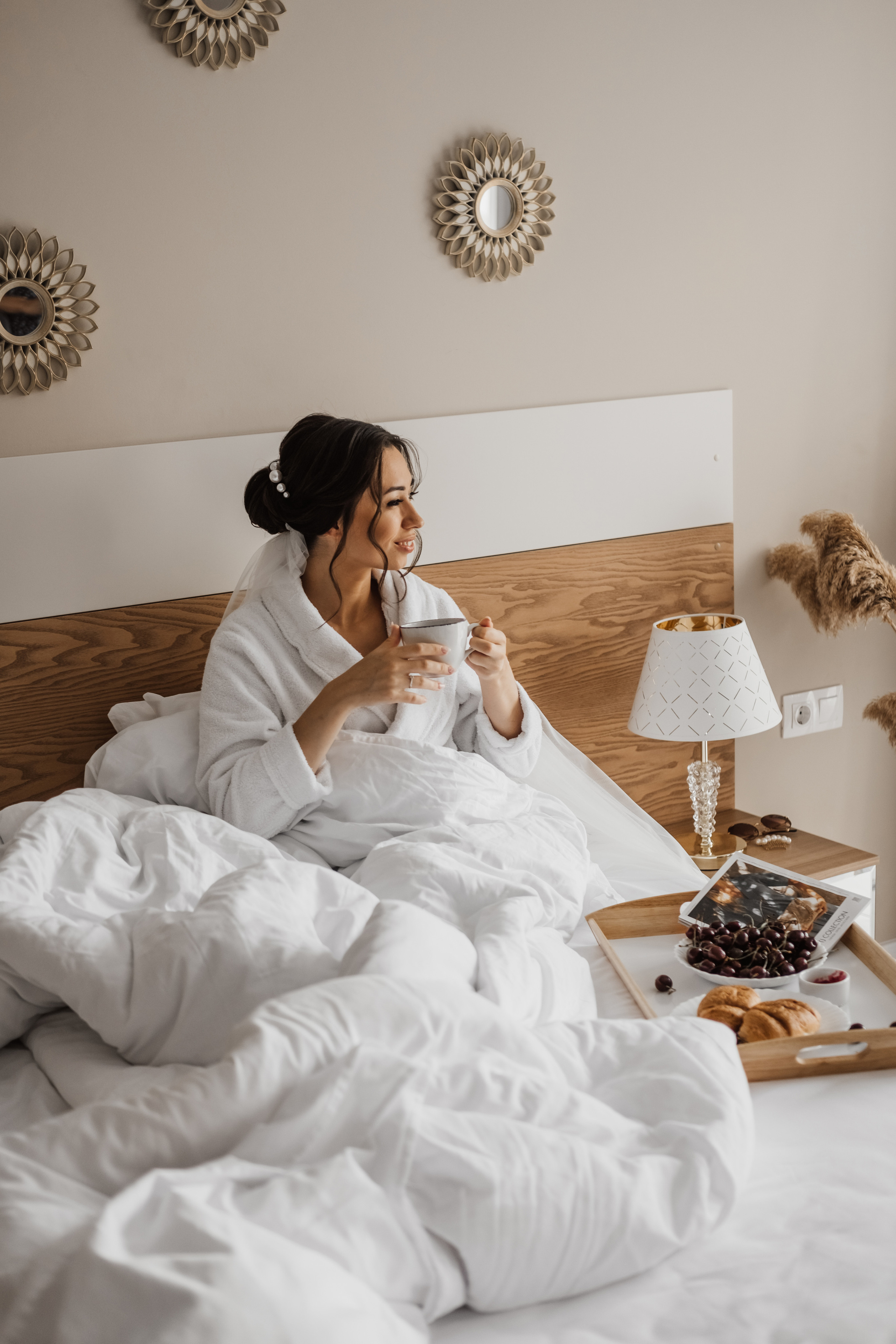Девушка утром в белоснежной кровати пьет тёплое кофе.