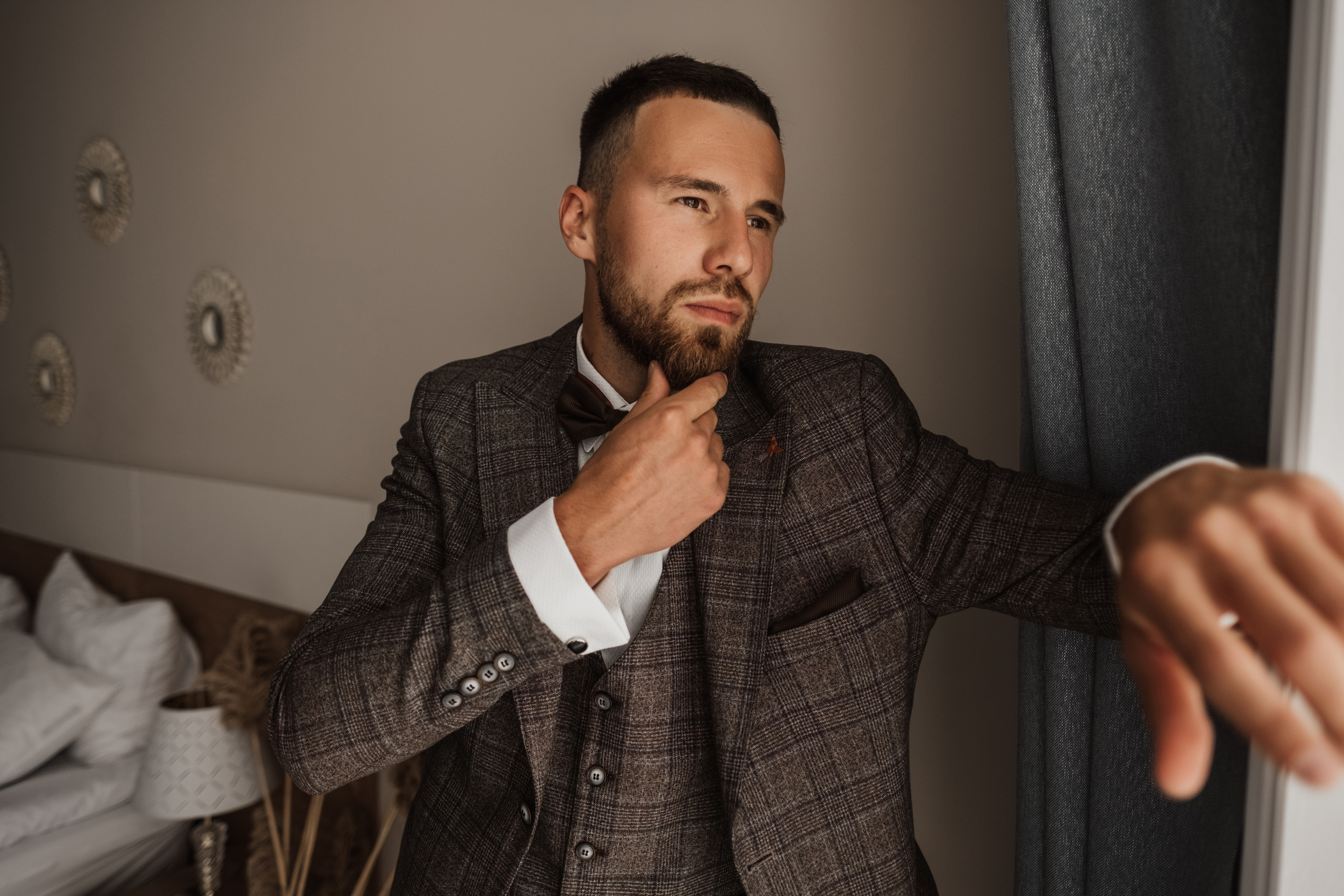 Молодой человек в костюме стоит и смотрит в окно.