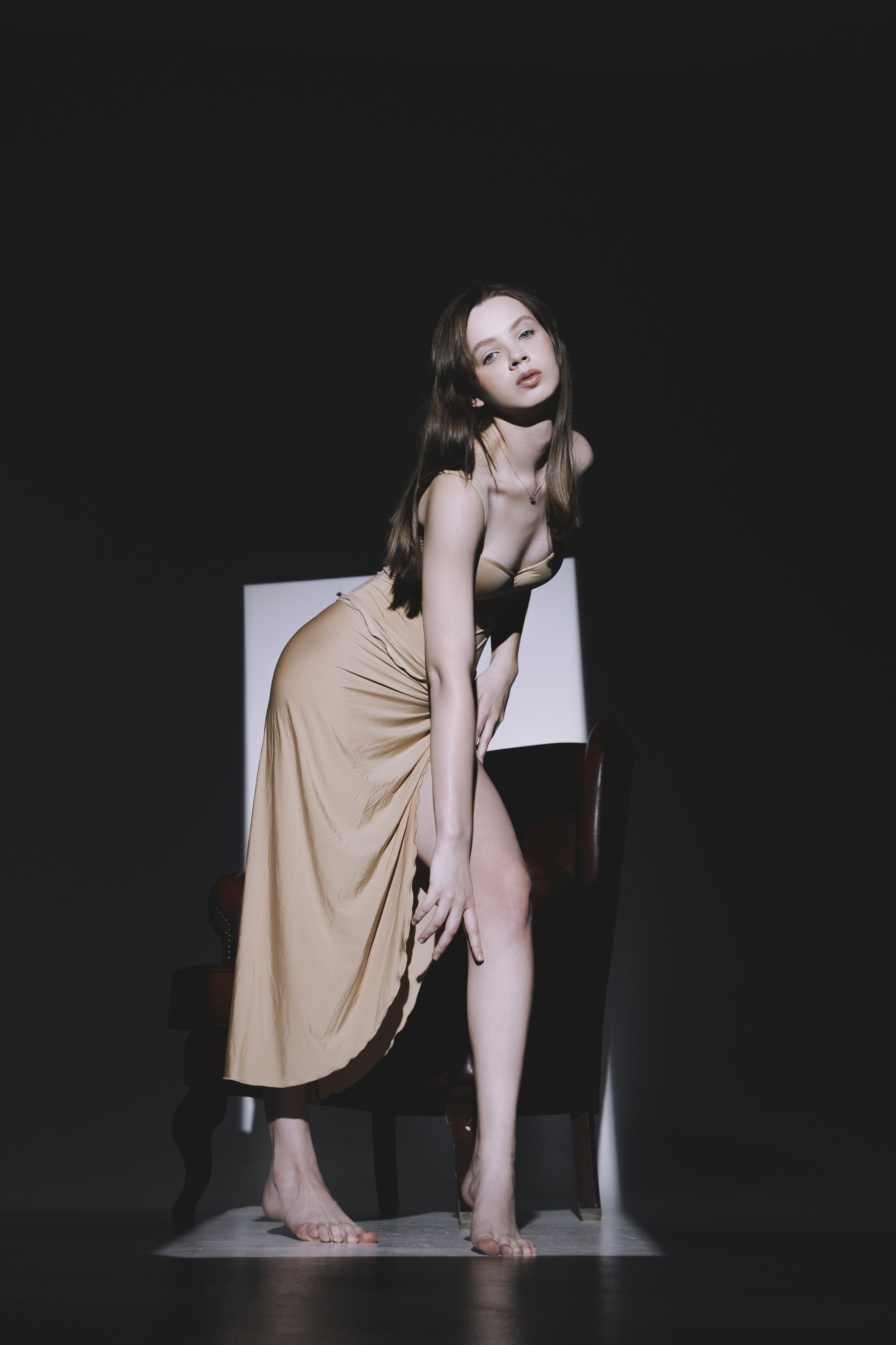 Фотосессия с драматическим освещением: девушка в элегантном платье запечатлена в момент задумчивости. Тёмный фон и акцентный свет создают кинематографический эффект.