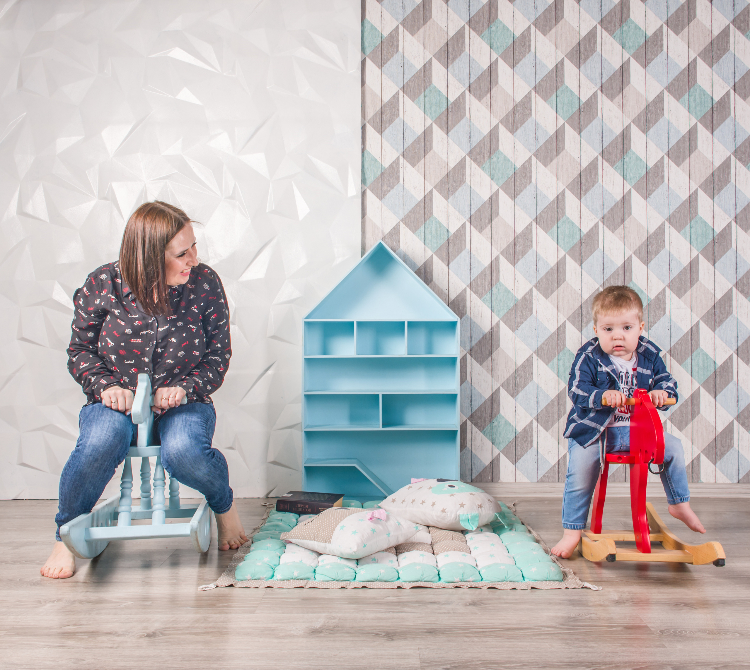 Мама и маленький сын в студии катаются на деревянных лошадках