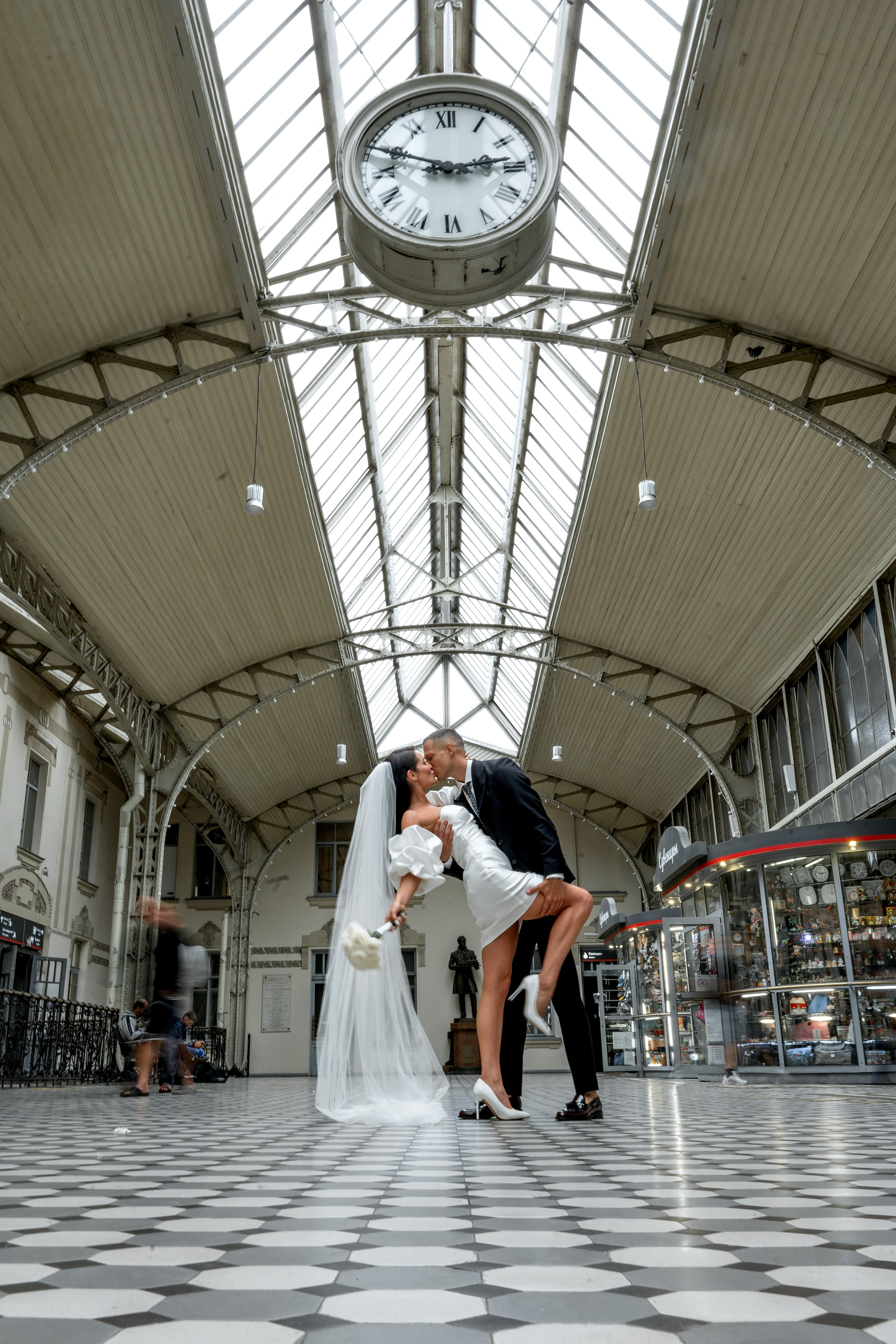 жених и невеста красиво целуются под часами на Витебском вокзале