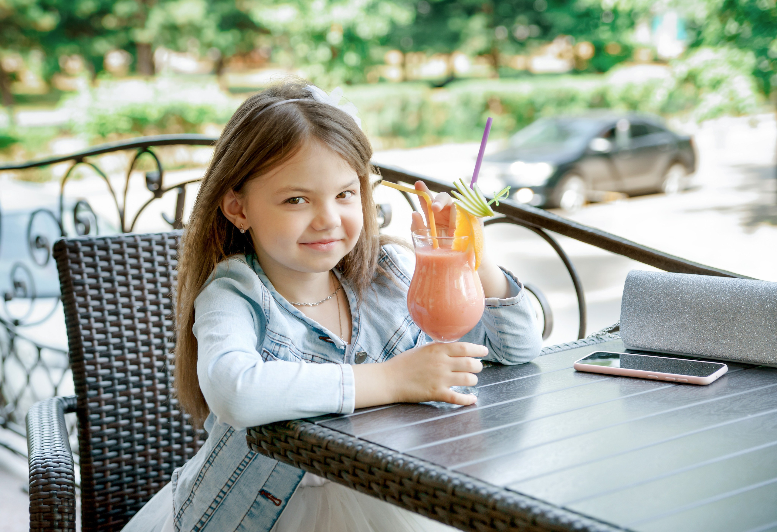 Детская фотосессия летом - девочка сидя за столиком в кафе с коктейлем