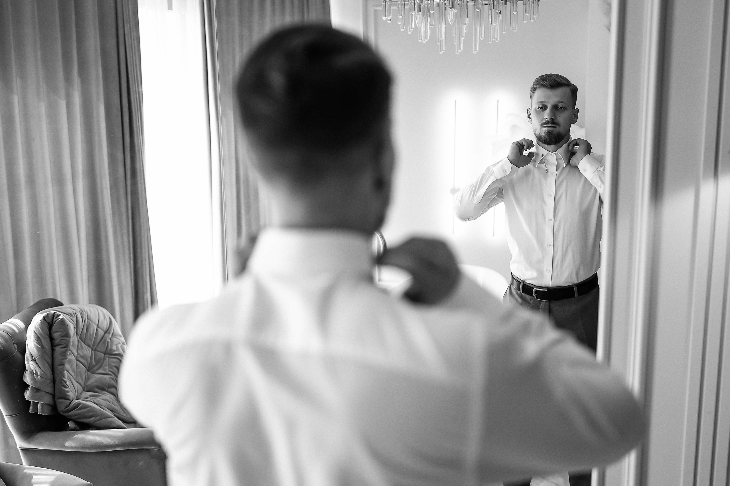 Жених собирается и смотрит в зеркало, поправляет рубашку