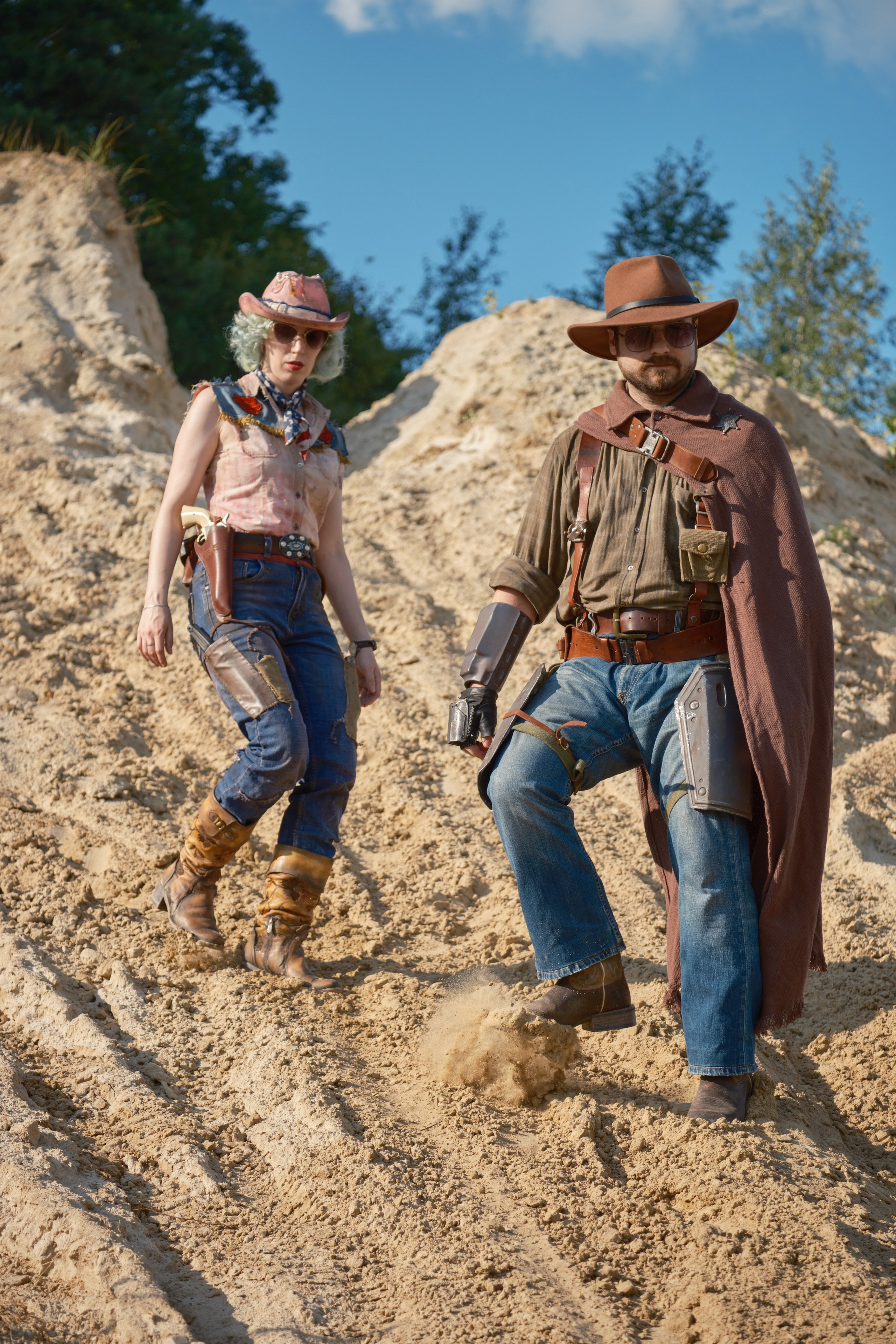 Мужчина и девушка в ковбойских шляпах спускаются с песчаных дюн в стиле пост апокалипсис