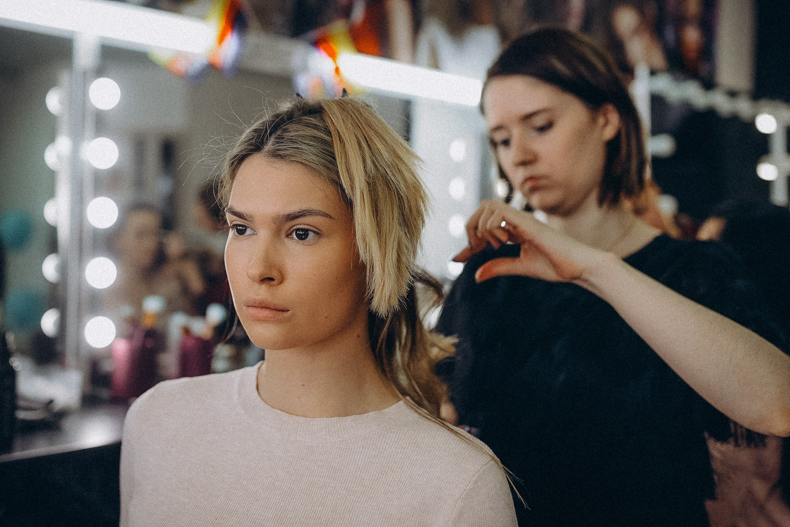 Стилист по волосам использует плойку для создания локонов участнице конкурса.