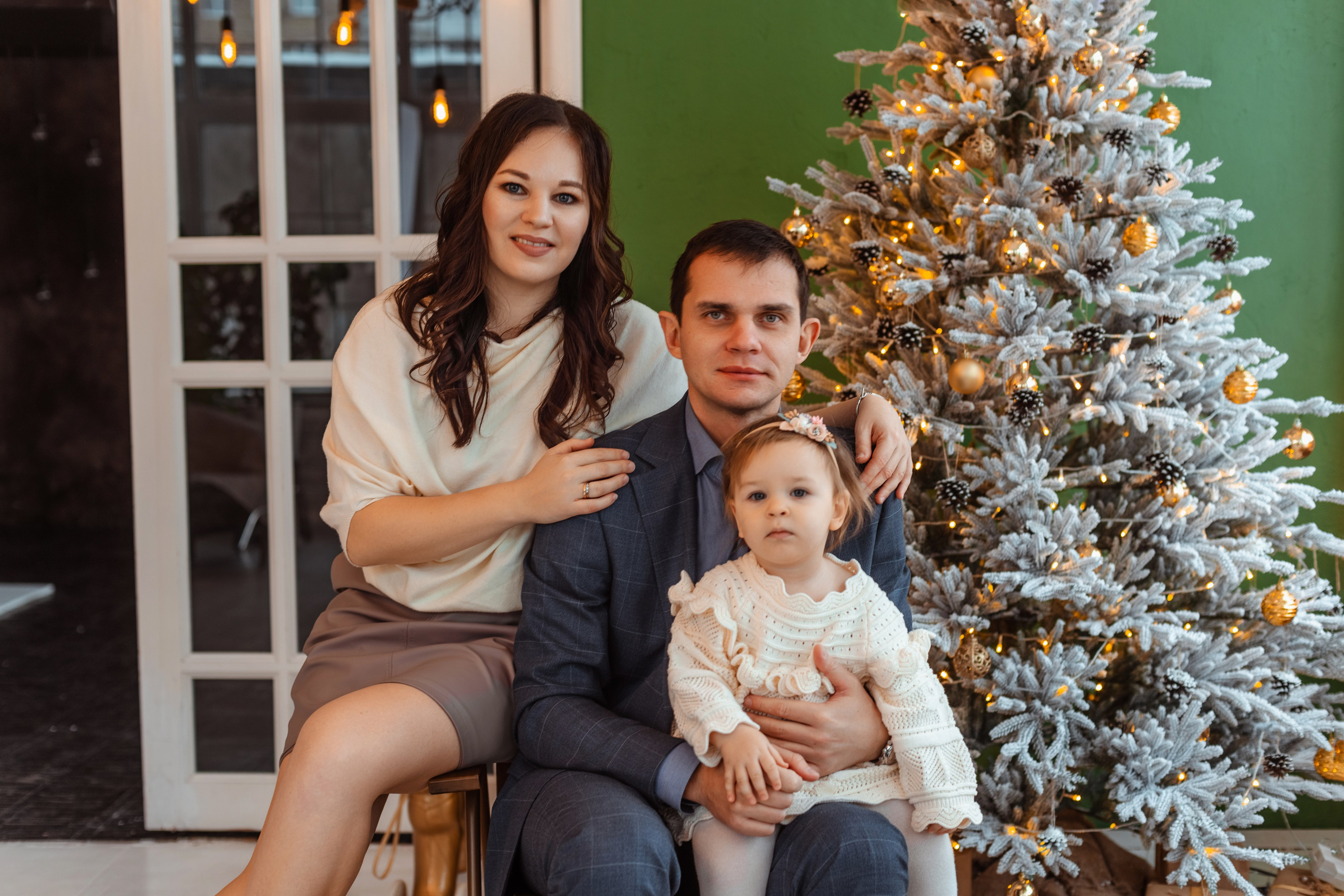  Семейная фотосессия на Новый Год: мама, папа и старший сын улыбаются на фоне елки.