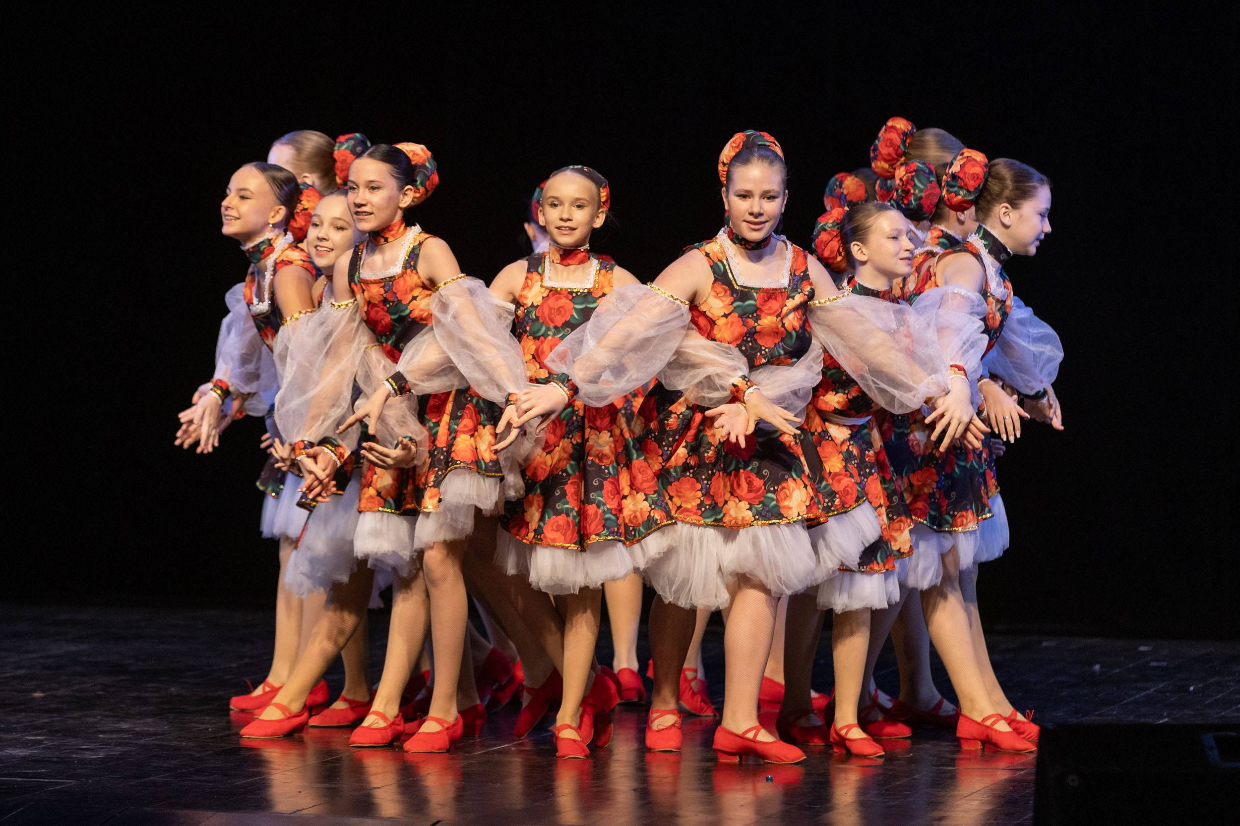 Фрагмент выступления танцевального коллектива девочек на темном фоне.