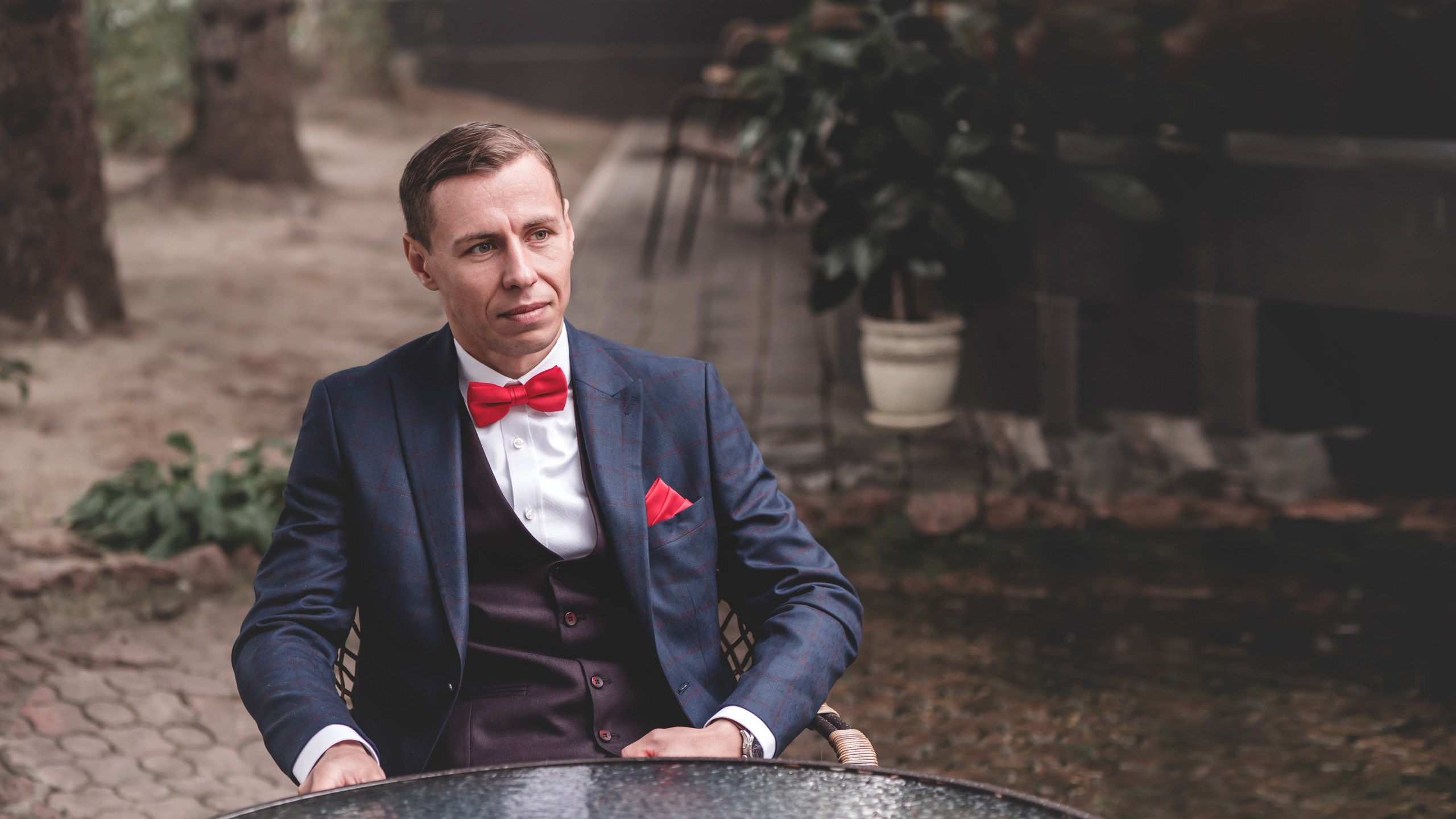 мужчина в строгом синем костюме в полоску и в красной бабочке. на нём белая рубашка и сидит он за столом.