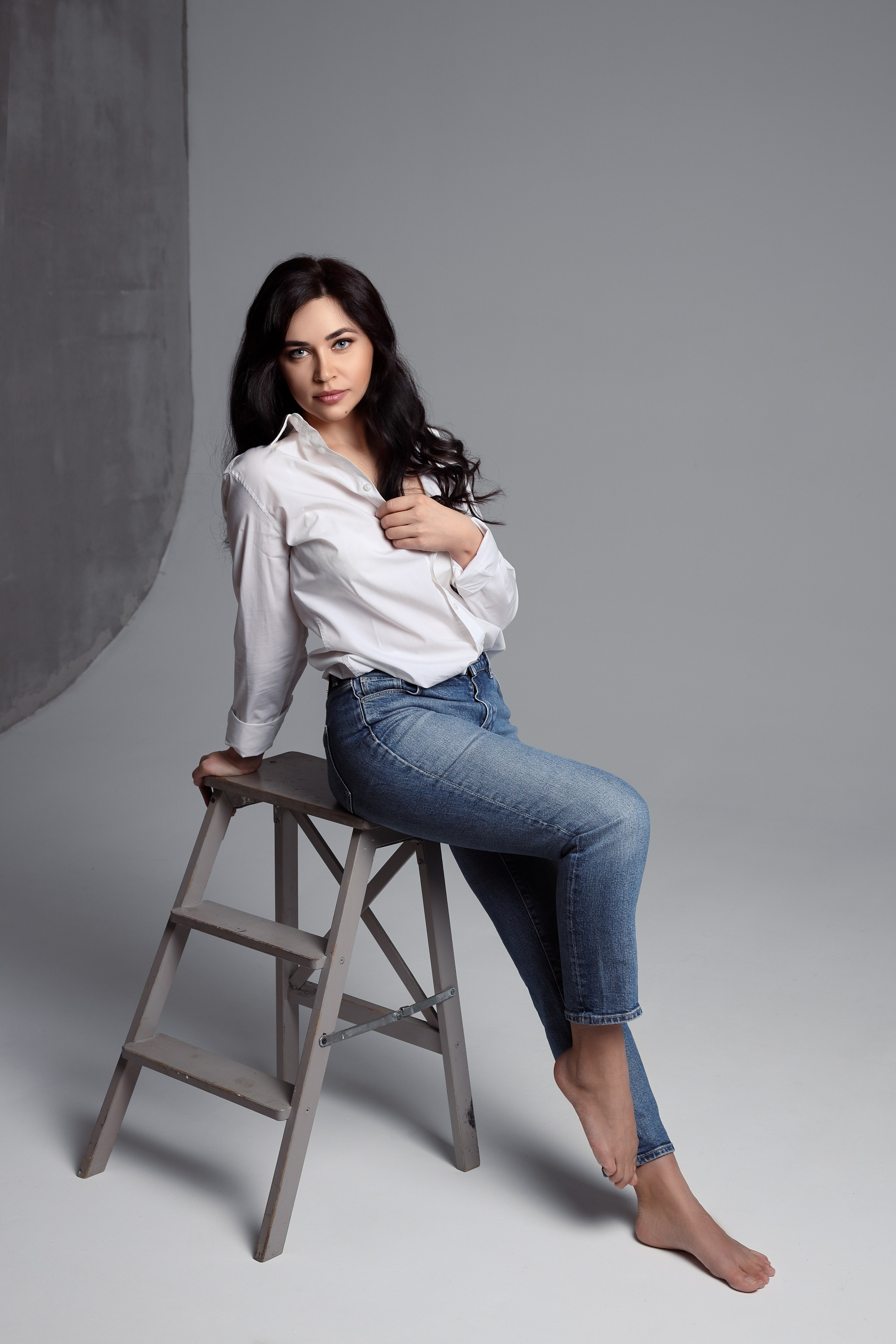 Девушка в джинсах и рубашке позирует на высоком стуле — лаконичная женская фотосессия в студии.
