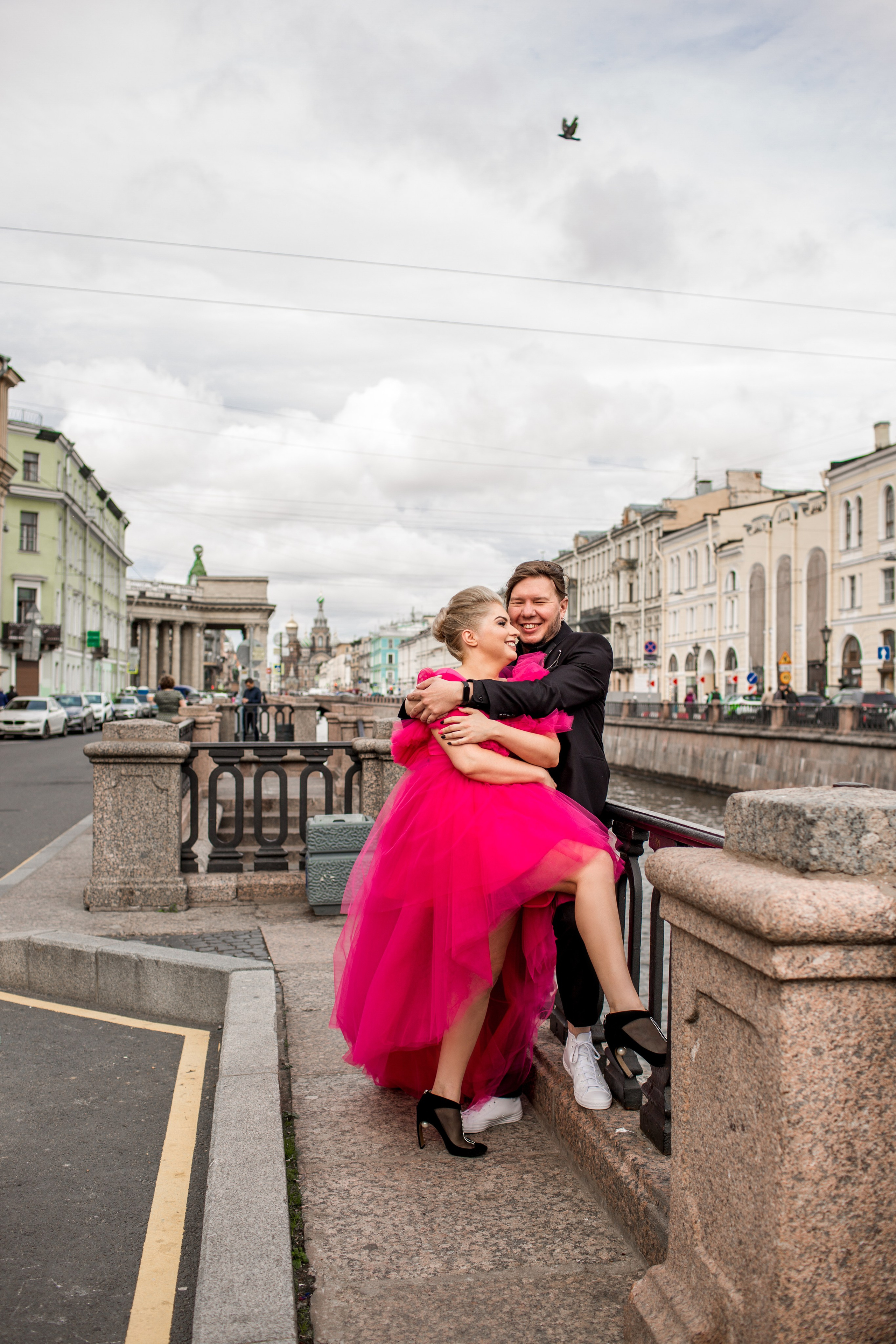 Свадебная пара в объятиях на фоне исторического здания, невеста в красном