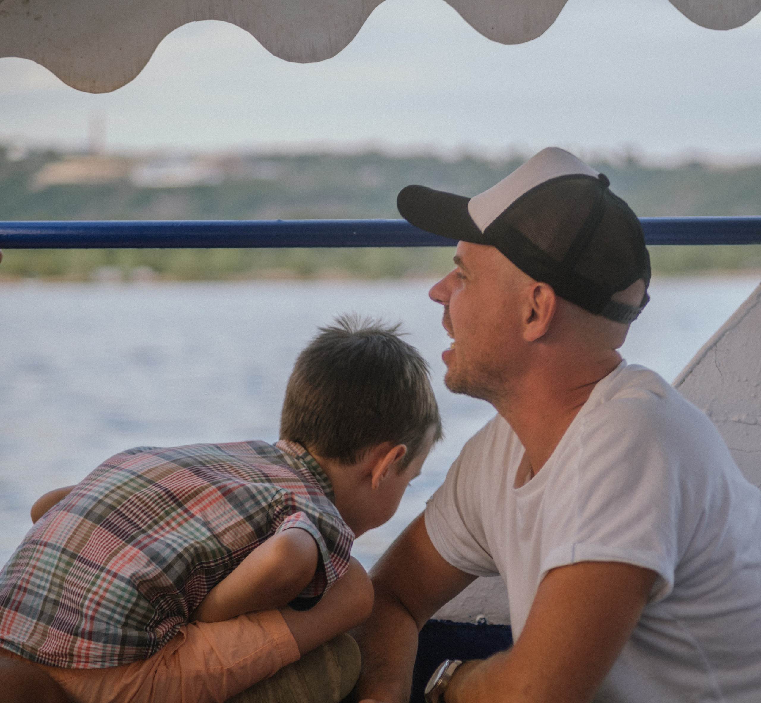 Сын прижимается к отцу в объятии на борту лодки — трогательный момент родительской любви на закате.