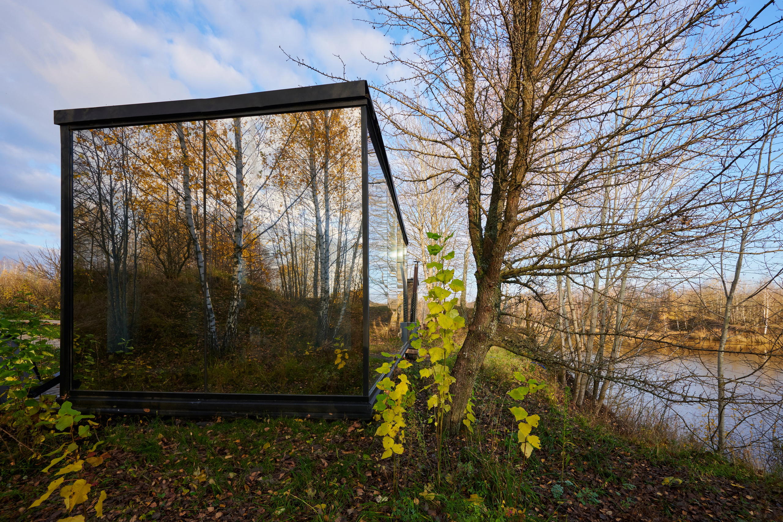 Стеклянный куб-домик среди деревьев, осенний свет.