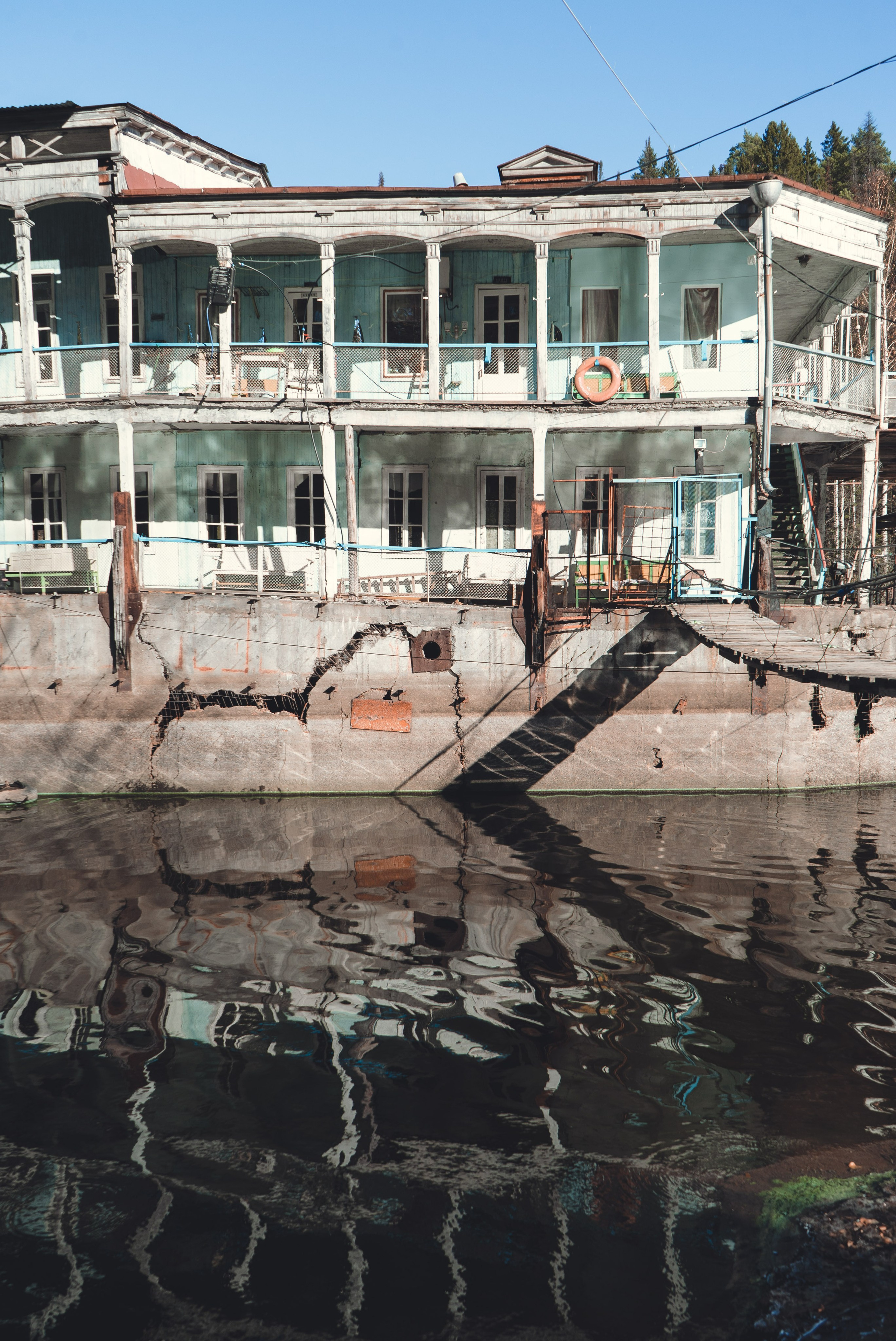 Заброшенное здание, виднеющееся на старинном берегу речной пароход, стоит на водоеме среди густого леса. Его фасад украшен колоннами и балконами, однако здание выглядит ветхим и запущенным: краска облупилась, металл покрыт ржавчиной. Вокруг голые деревья и хвойные леса, что создает ощущение уединенности и застенчивости.